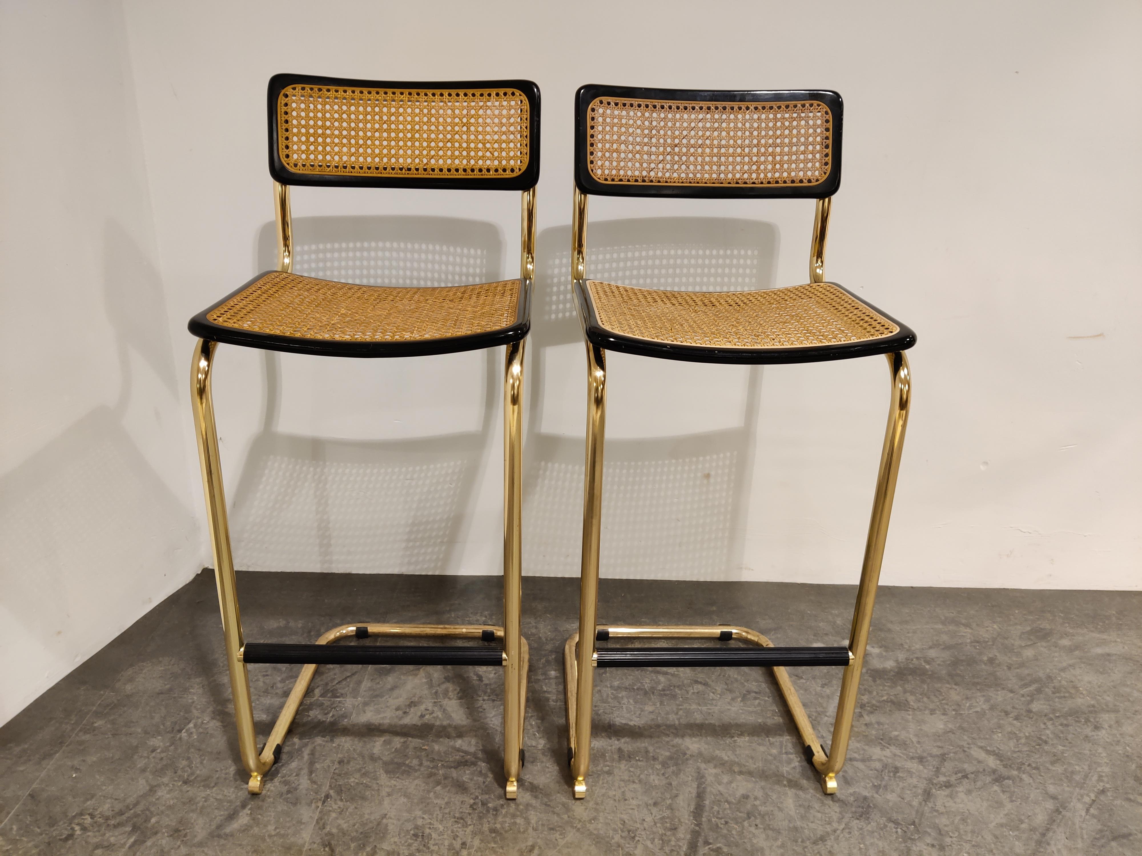 Set of 2 Marcel Breuer style Bauhaus design bar stools with brass frames.

Tubular brass frame with cane seats and black lacquered wood, labeled 'made in italy'

All in very good condition.

Protected foot rests.

Dimensions:
Height:
