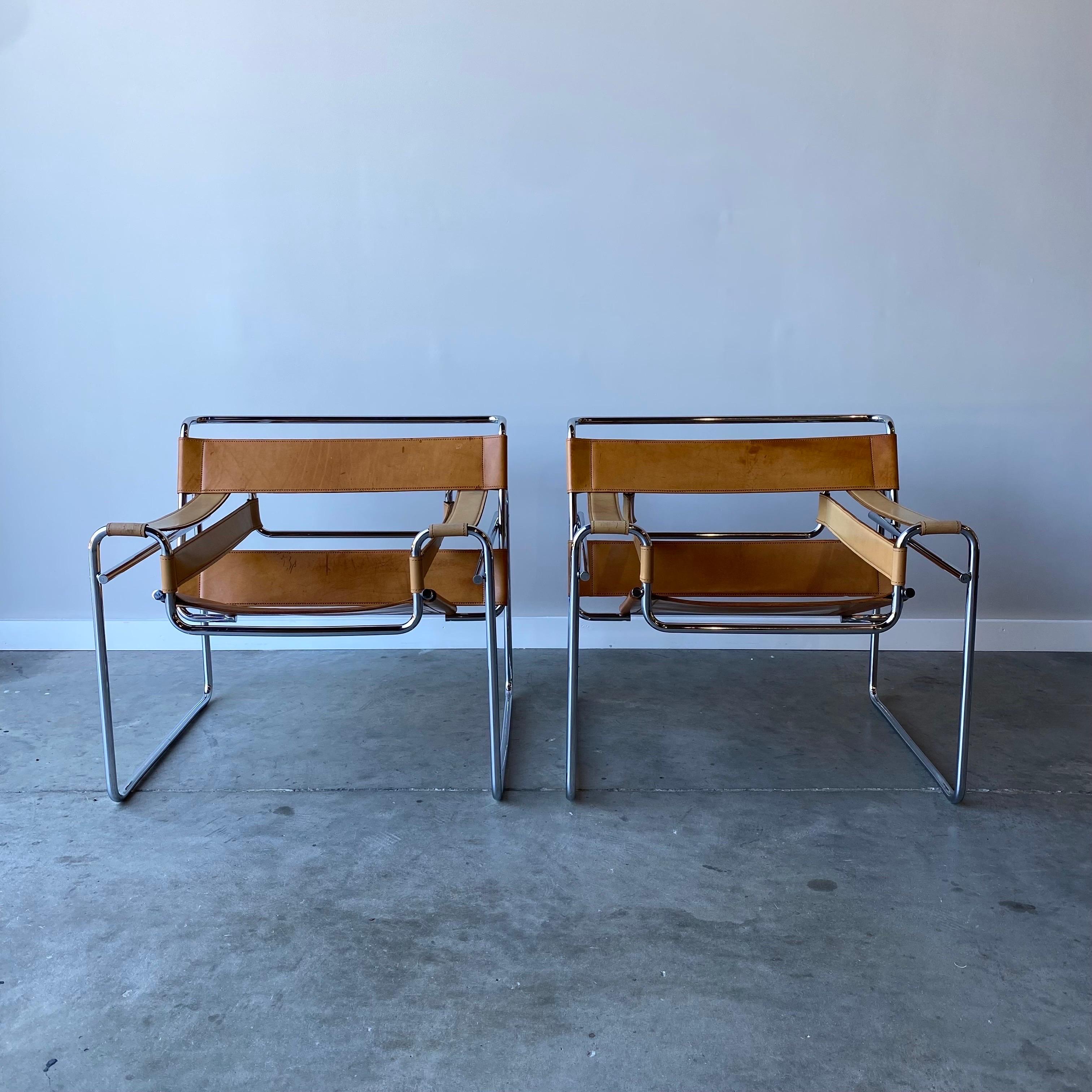 A pair of tan leather chairs likely by Gavina.   These are marked “made in Italy” and are high quality construction with welded the caps.  The chrome frames are in very good condition with the leather straps showing lots of scrapes and stains along