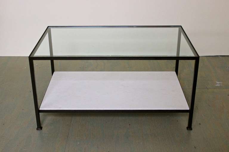 Cette table basse classique présente un cadre en fer avec une finition bronze appliquée à la main, un plateau en verre transparent et une tablette inférieure en calcaire. Il s'agit d'un échantillon de sol de notre ligne discontinuée Reeditions.