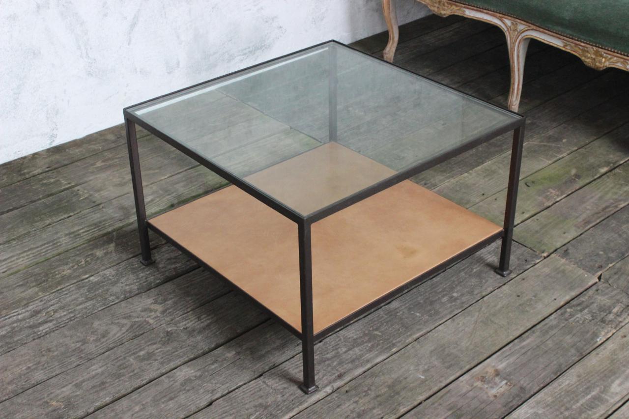 This contemporary coffee table features a square iron frame with a bronze paint finish, adding a touch of modernity to your living space. The top shelf is made of clear glass, providing a sleek and transparent surface, while the bottom shelf is