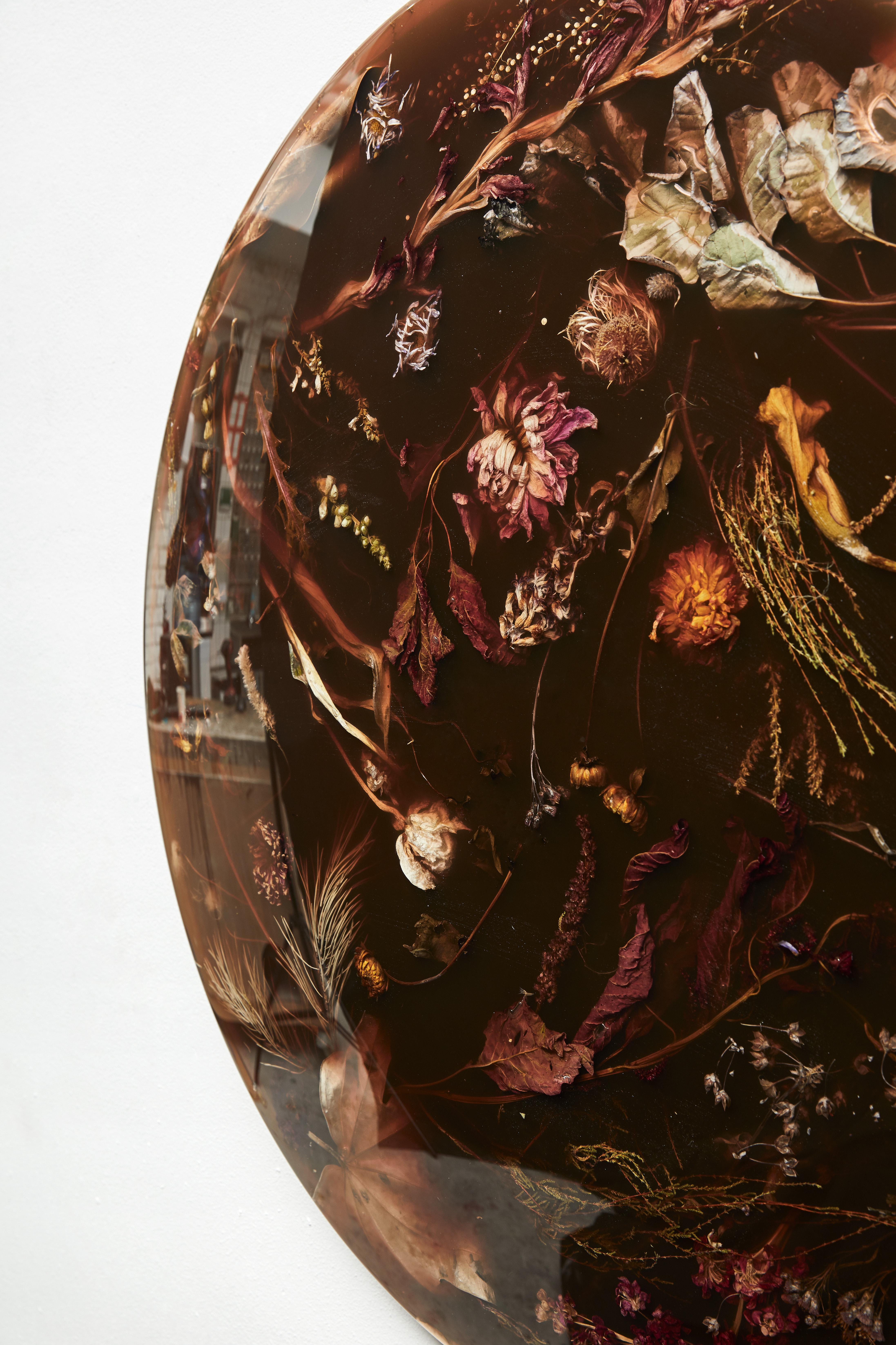 Faisant partie de la collection Flora de Marcin Rusak, la suspension murale Flora Lens 65 constitue une pièce décorative unique qui s'adapte à une variété de contextes. Réalisée à partir de fleurs jetées soigneusement immergées dans la résine, cette