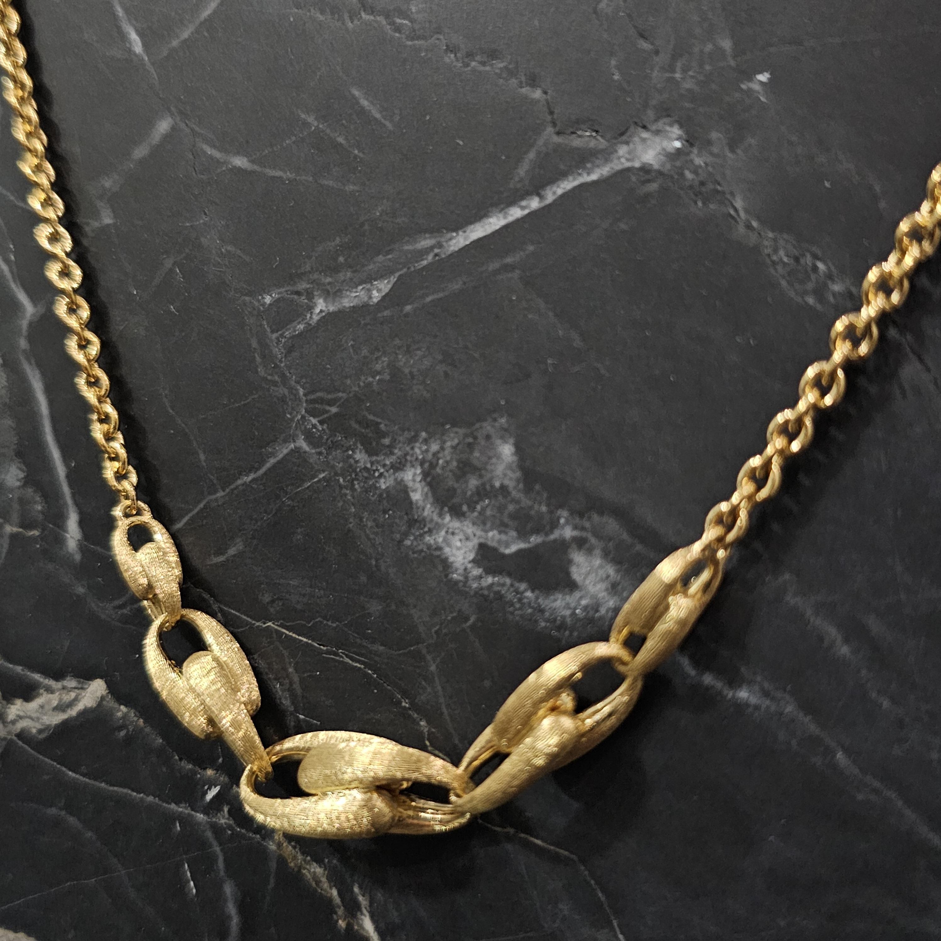 Questa collana a catena di Marco Bicego è realizzata in oro giallo 18 carati e presenta un design audace ed elegante. La collana è caratterizzata da una serie di maglie allungate e strutturate che formano un elemento centrale di grande effetto e che