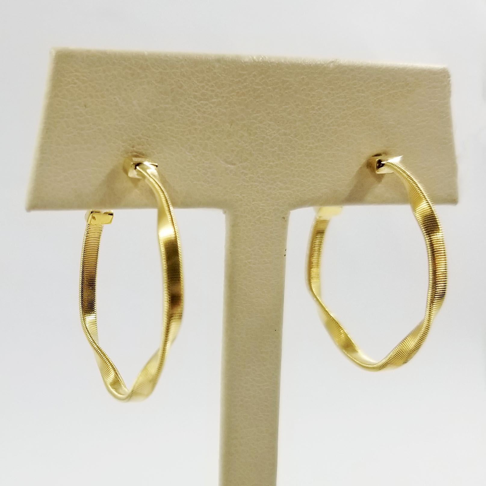 These twisted and textured hoop earrings are crafted in 18 karat yellow gold. The tops are signed Marco Bicego. The earrings feature a post and friction back closure. Diameter of hoop is approximately 1 inch. Finished weight is 5 grams. MSRP is