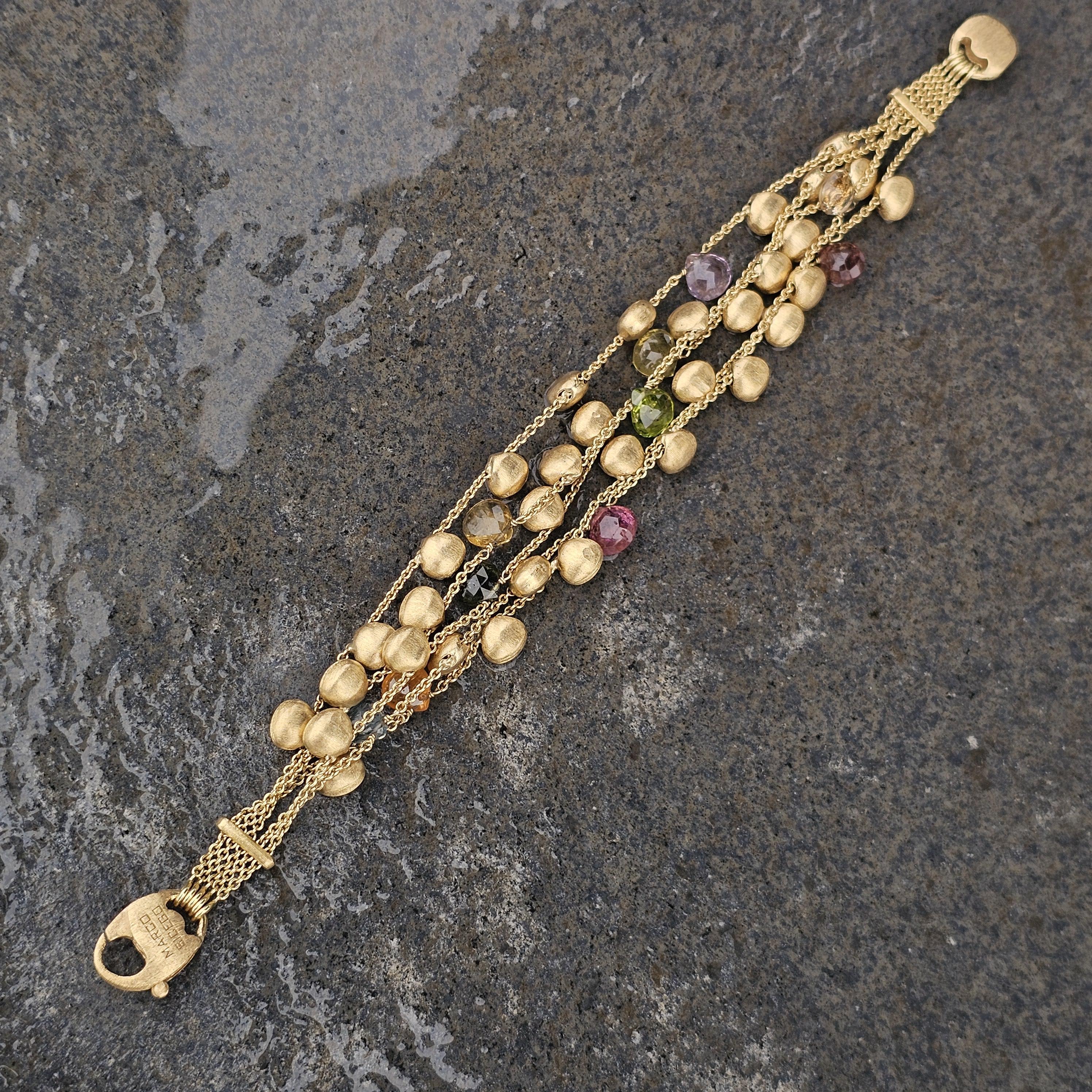 This exquisite Marco Bicego bracelet is a captivating addition to any jewelry collection. Crafted from 18k yellow gold, it features a unique design with textured gold beads interspersed with vibrant gemstones. The 5 multi-strand chain adds depth and