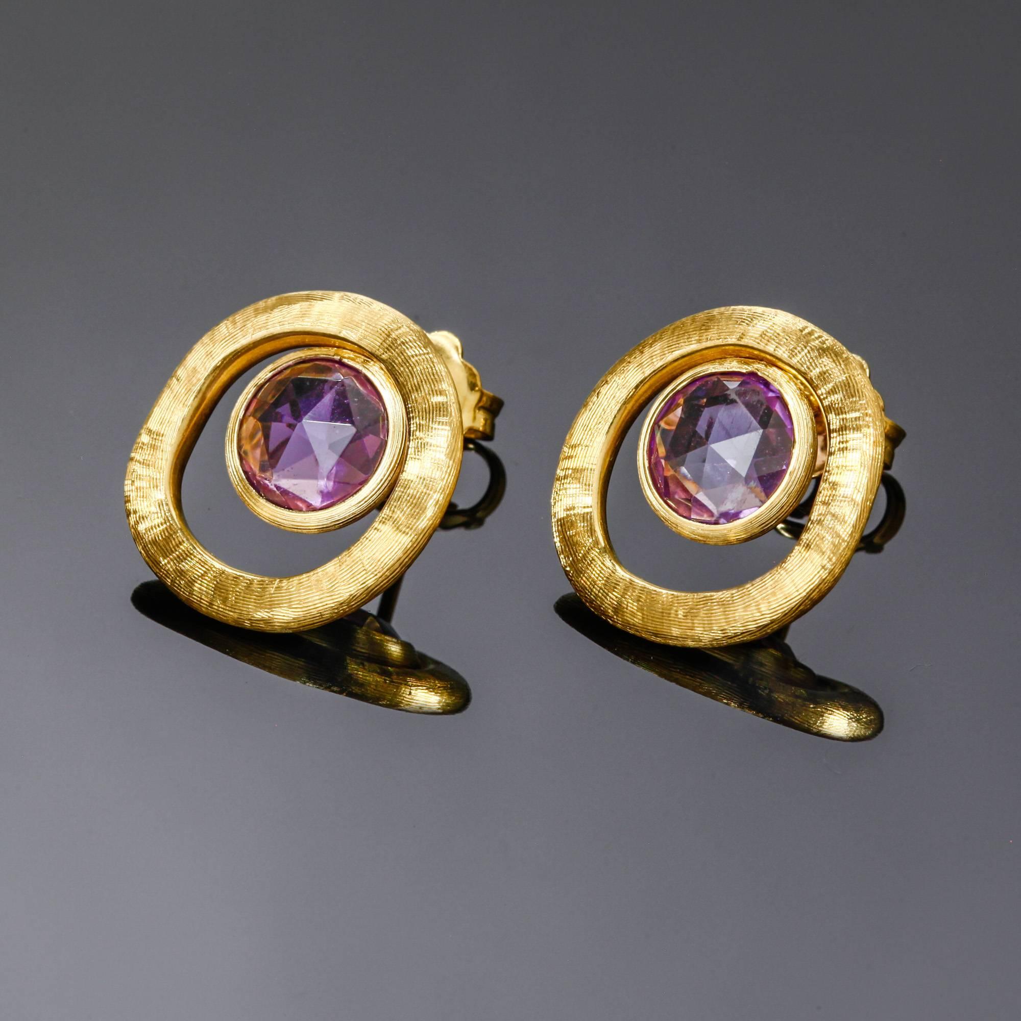 This pair of Marco Bicego amethyst earrings from the Jaipur Color collection is set in 18k yellow gold that was hand engraved by Italian artisans. These earrings have never been worn. Each earring measures approximately 12mm wide. 