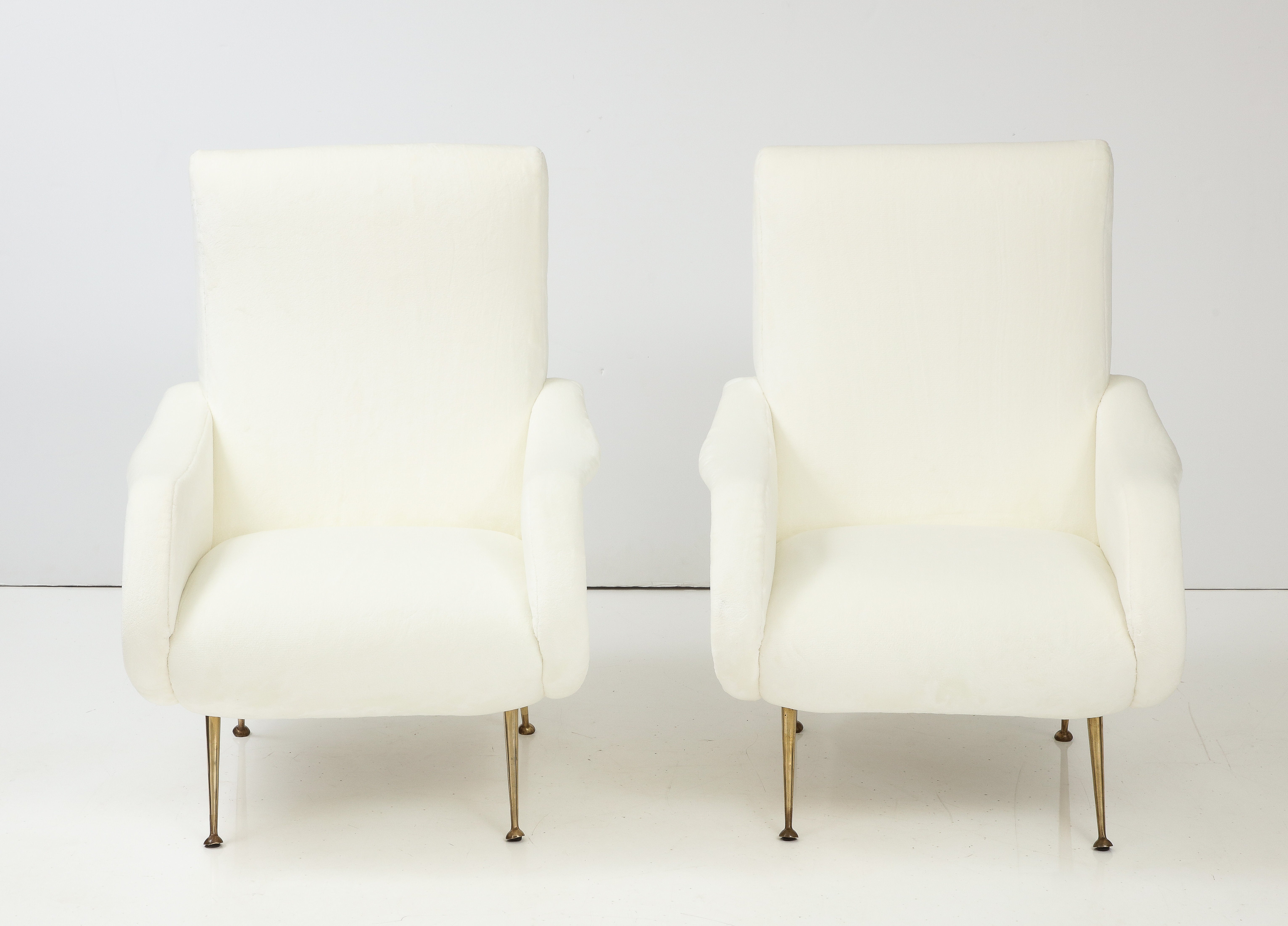 A pair of Italian mid-century modern lounge chairs, This pair have been fully restored and newly upholstered in our professional studio in a creamy white faux fur fabric with elegant tapered brass and metal legs.   The curvaceous and elegant lines