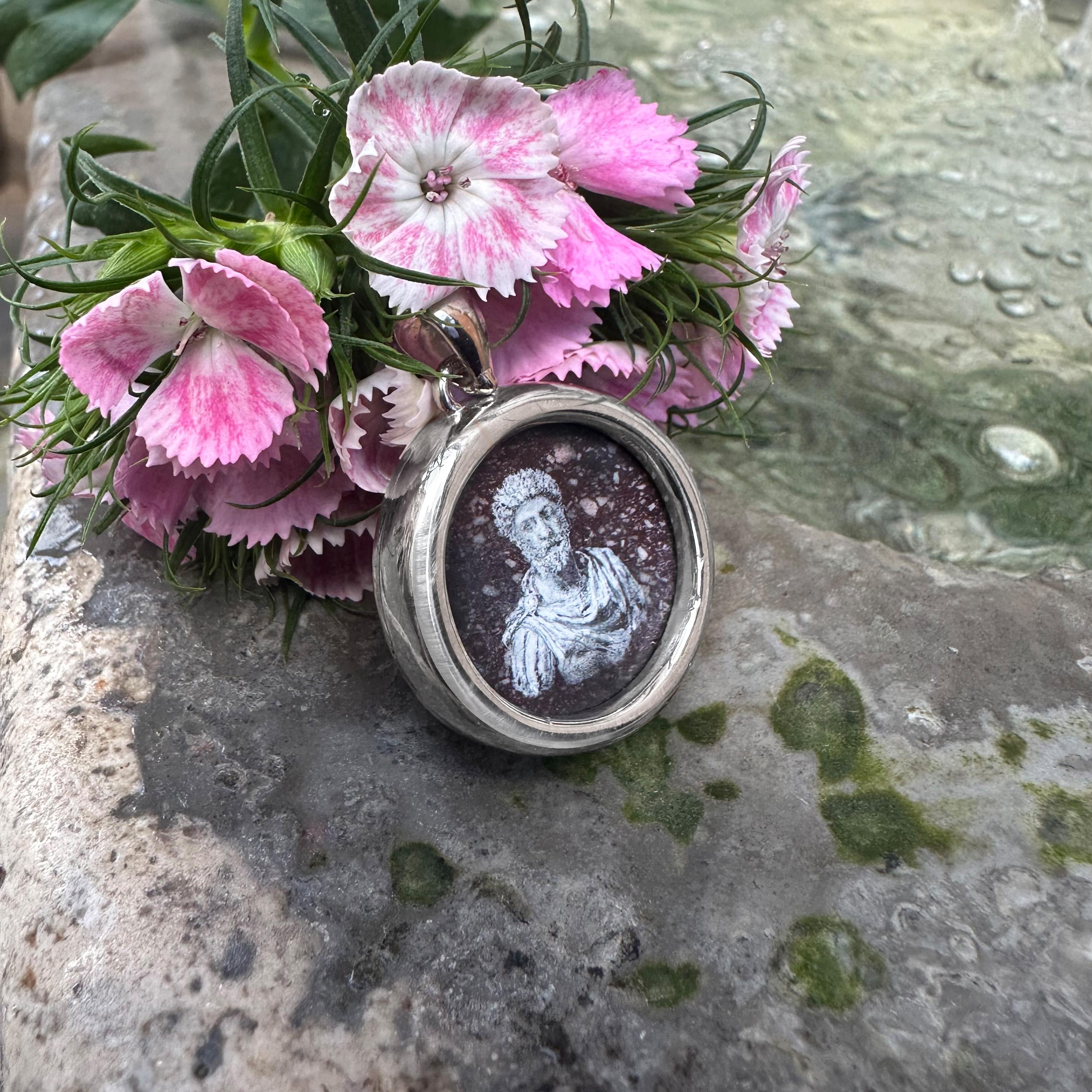 Questo ciondolo presenta una rappresentazione dipinta a mano dell'imperatore romano Marco Aurelio, abilmente realizzata dall'artista Tommaso Rossi su porfido rosso. Incastonato in argento massiccio, celebra Marco Aurelio, il re filosofo e simbolo di