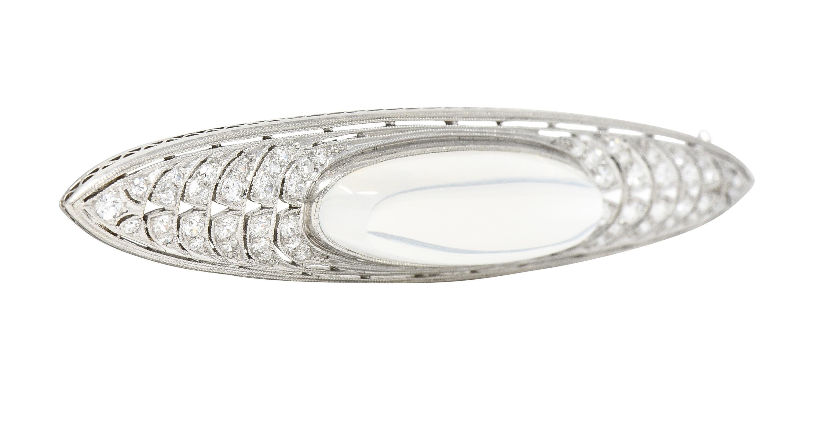 Centering an elongated sugarloaf-shaped moonstone cabochon measuring 27.0 x 9.0 mm 
Translucent colorless in body with white adularescence - bezel set
Featuring a pierced arching surround bead set with rows of graduated old European cut diamonds