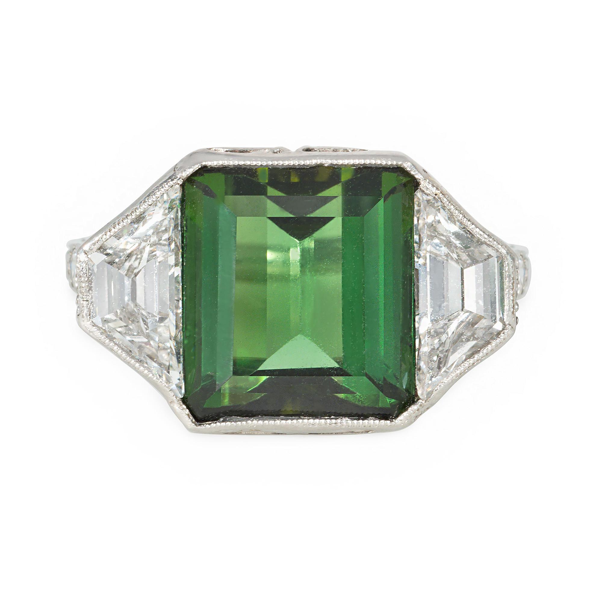 An Art Deco tourmaline, diamond, and platinum ring featuring an emerald-cut green tourmaline center flanked by trapezoid diamonds, with diamond-set shoulders and open scrolled foliate work in the gallery, in platinum.  Marcus & Co.  Atw tourmaline