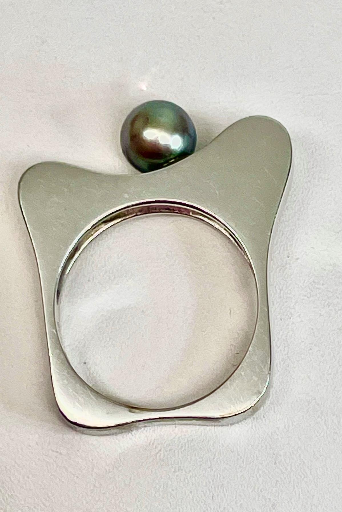 This ring is art. Whimsical shaped 14kt. White Gold Black Pearl ring accented with 3 Round Brilliant Natural Diamonds weighing a total of 0.09 ct. Clarity is SI1, Color G-H. The 7mm Natural Black Akoya Pearl appears to have ridden down the hump to