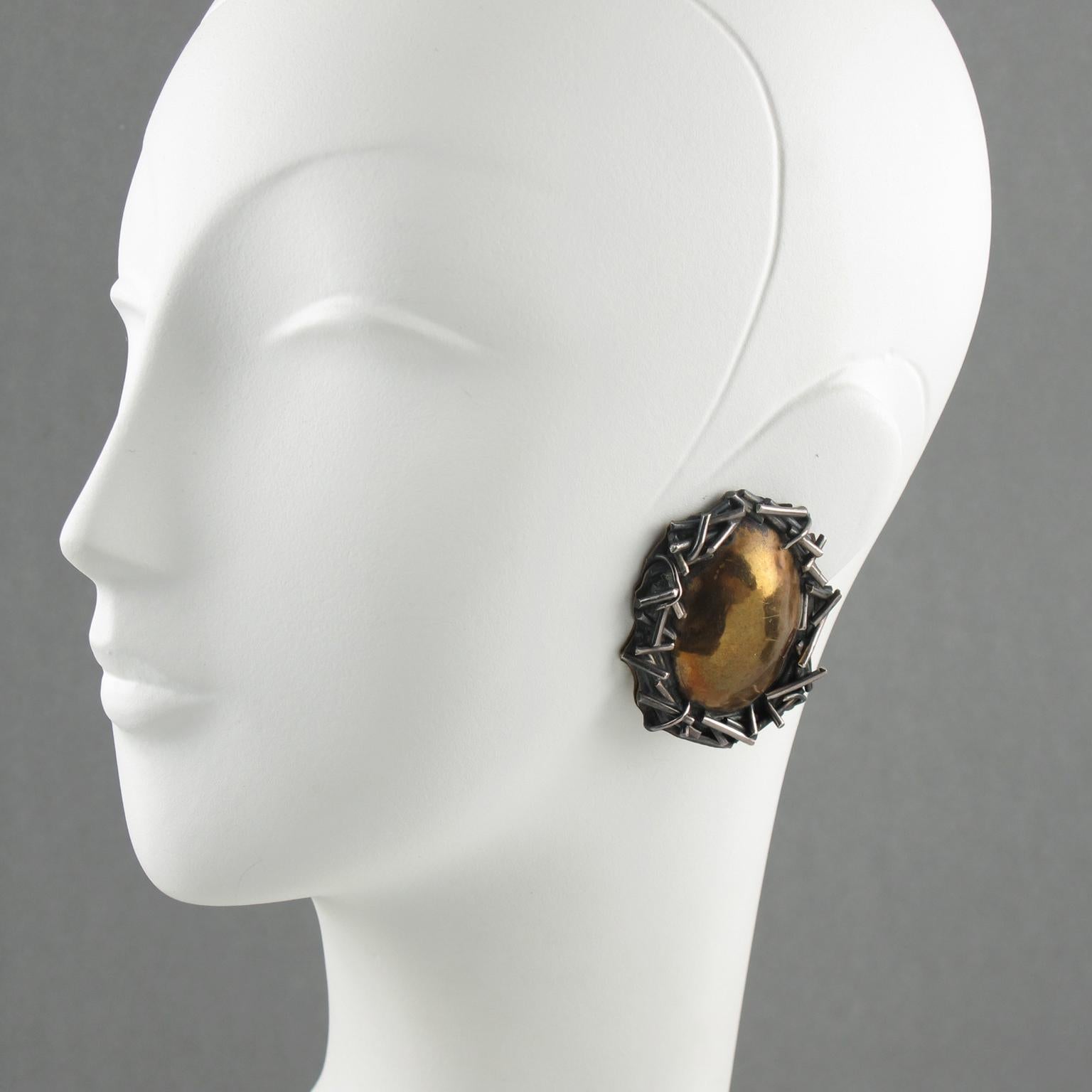 American designer Margaret Ellis created these stunning artisan handcrafted limited edition, massive clip-on earrings. The brutalist design has a sterling silver stylized crown of thorns and a large domed center in gilded bronze. One earring is