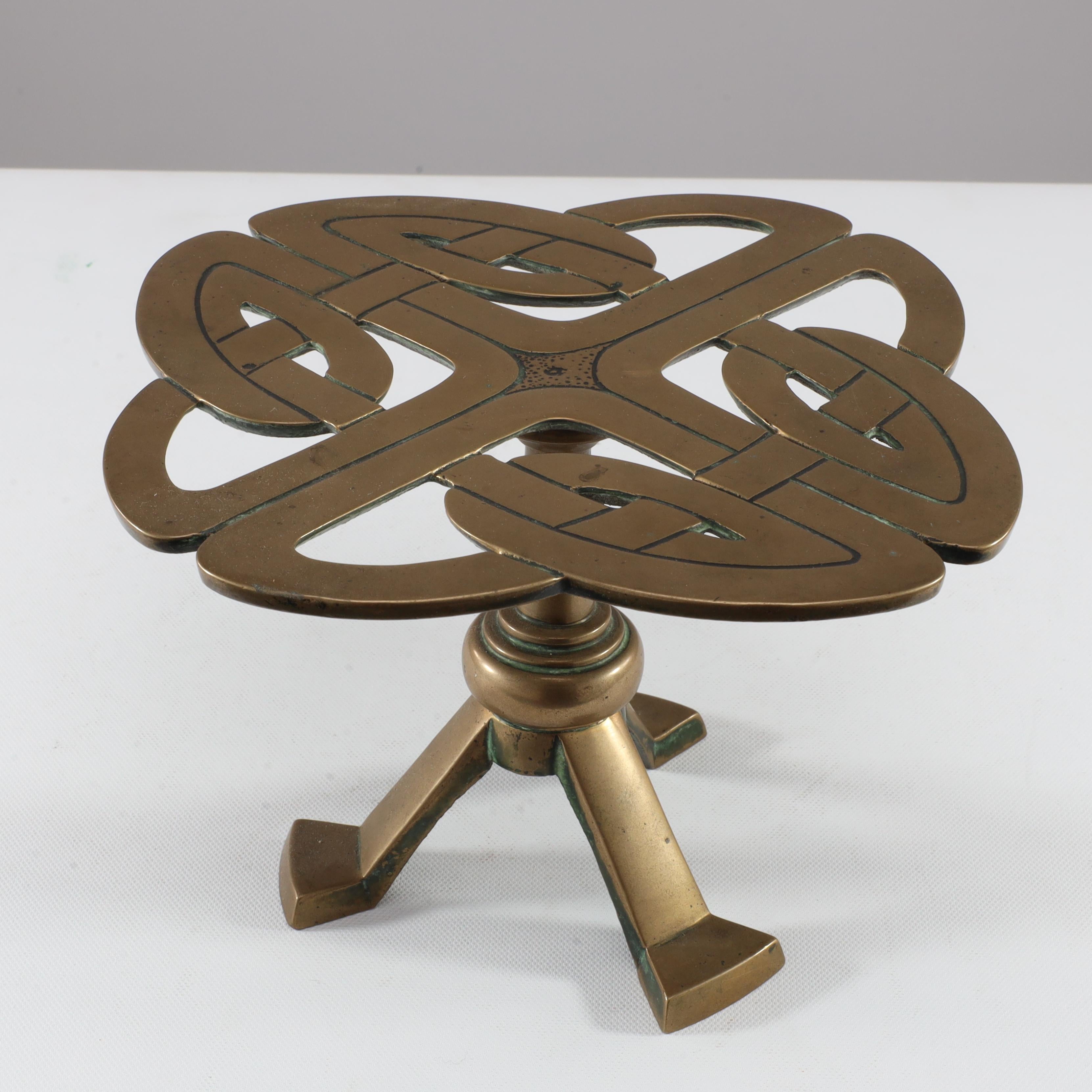 A good stylish Glasgow School brass trivet attributed to Margaret Gilmour with stylized Celtic interlaced details on three angled legs with out swept feet.