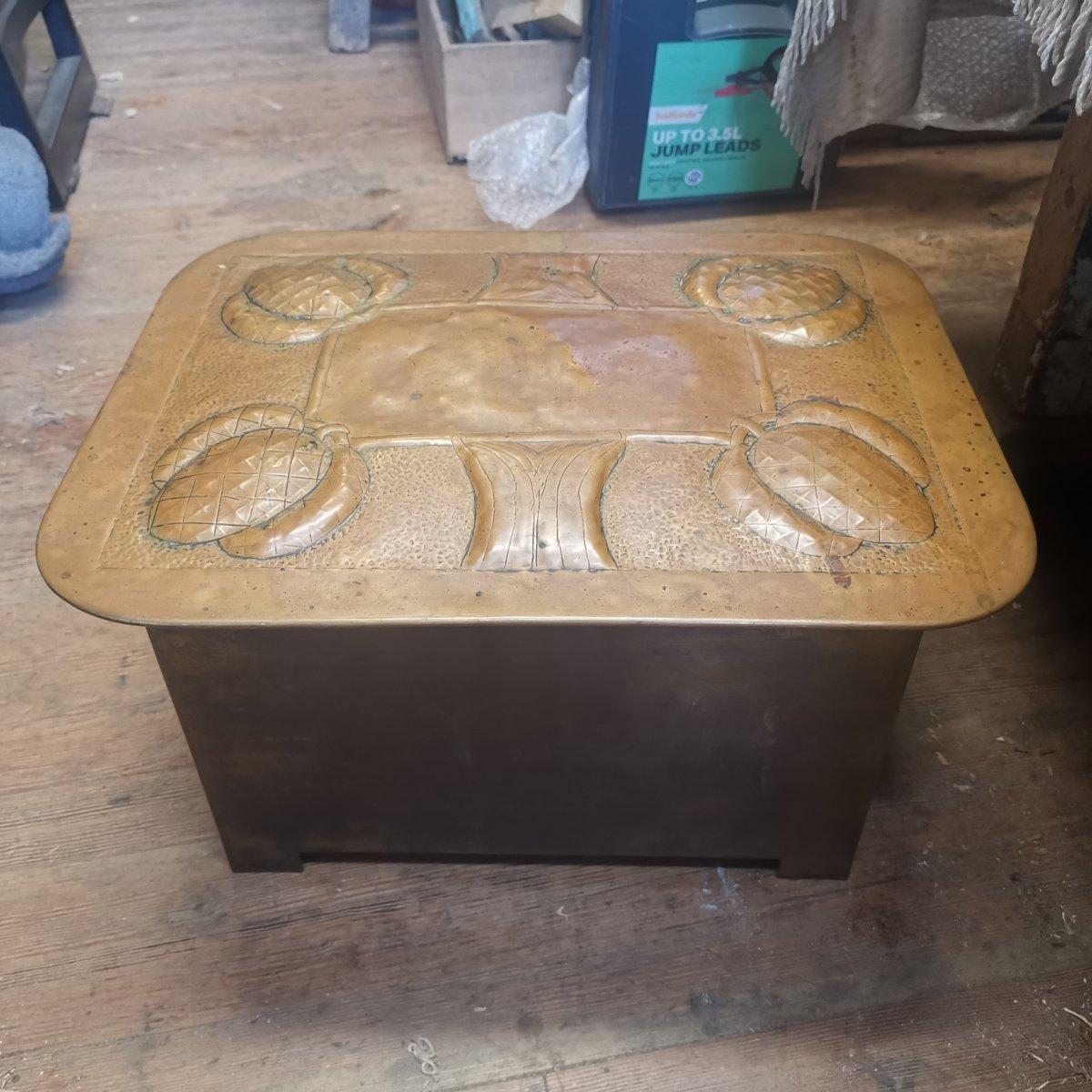 Magaret Gilmour School.
A Scottish School Arts & Crafts brass coal box with stylized thistle and leaf decoration, with large ring pull handles to each side framed around by further floral decoration, stood on triangular feet typical of the Gilmour