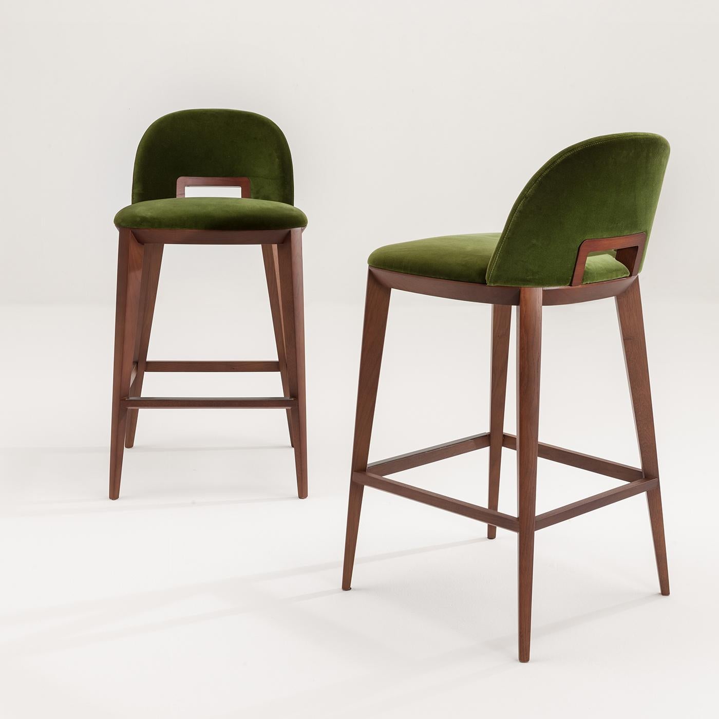 Le tabouret Margaret, en velours vert, a des pieds longs et fins qui se croisent avec l'assise et le dossier, ce qui lui confère harmonie et attrait. Avec un cadre et une poignée en chêne, le bois peut être teinté en palissandre, teck, wengé, noyer