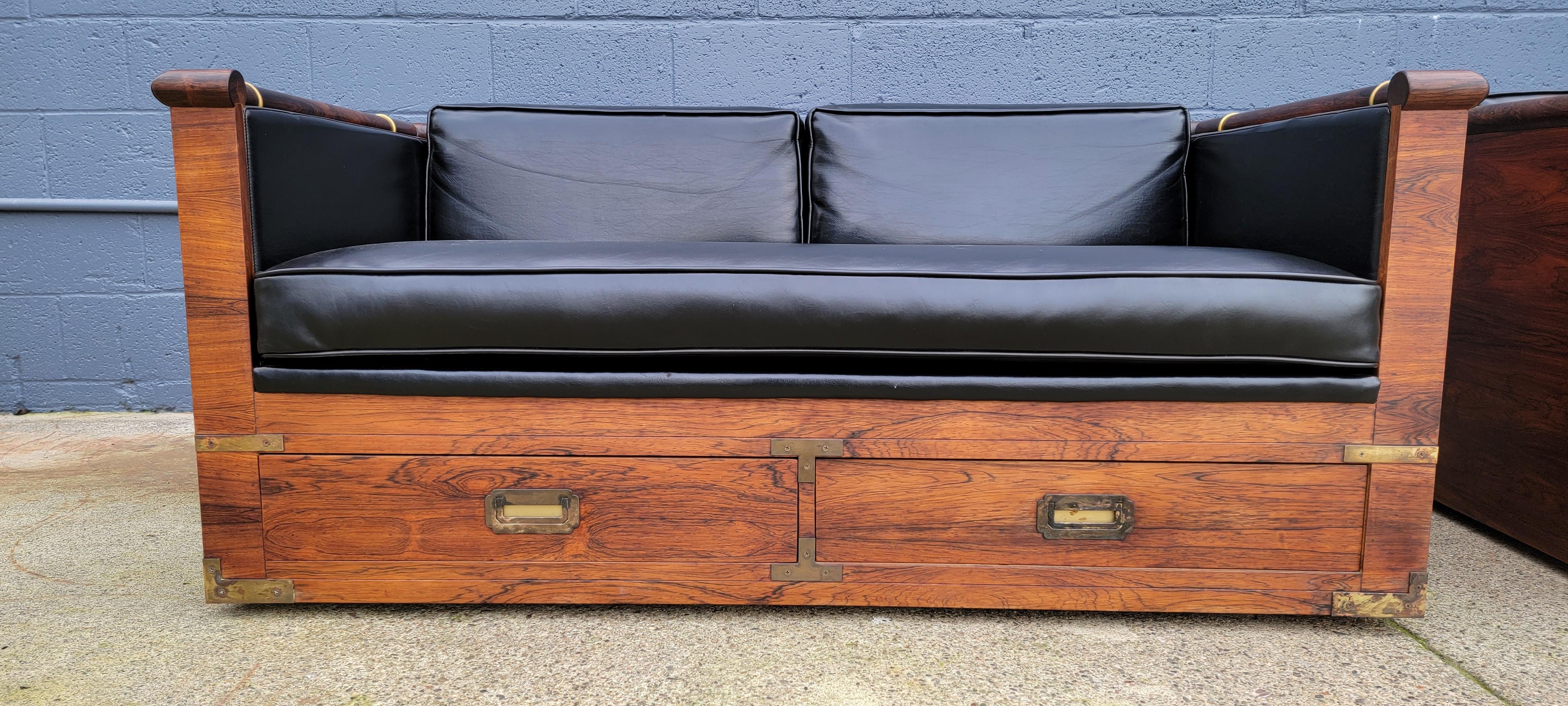 Exceptional matched pair of Campaign style rosewood sofas by Marge Carson. Deep, rich glow to original finish with beautifully figured wood grain. Brass mounts and handles. Each sofa features two drawers for storage and castors for easier moving.