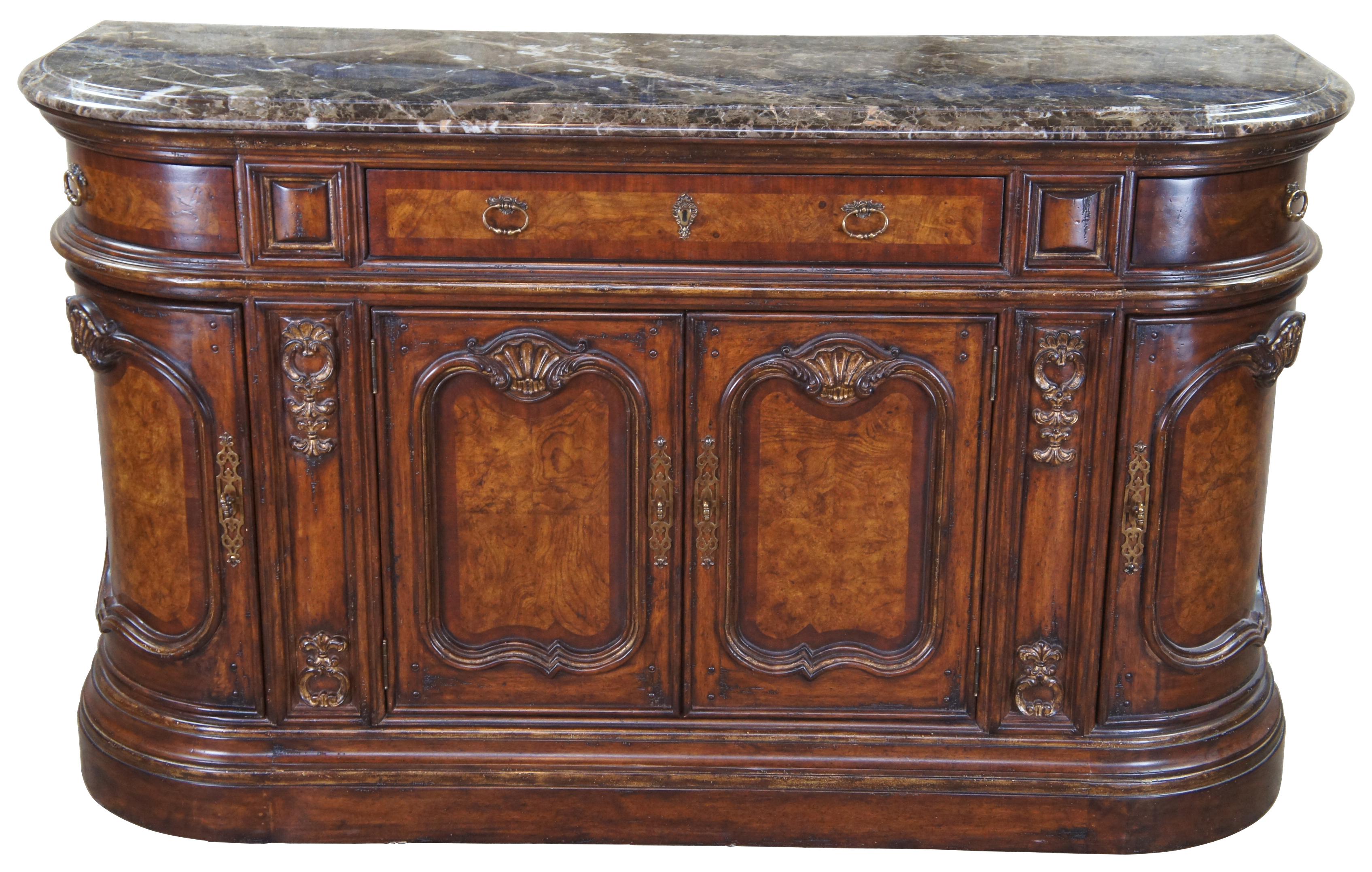 Baroque Revival sideboard by Marge Carson. Crescent or D shaped with a beautiful ash burl and golden scalloped trim. Features a marble top, brass hardware, silverware drawer and plenty of accessory storage. Measure: 72