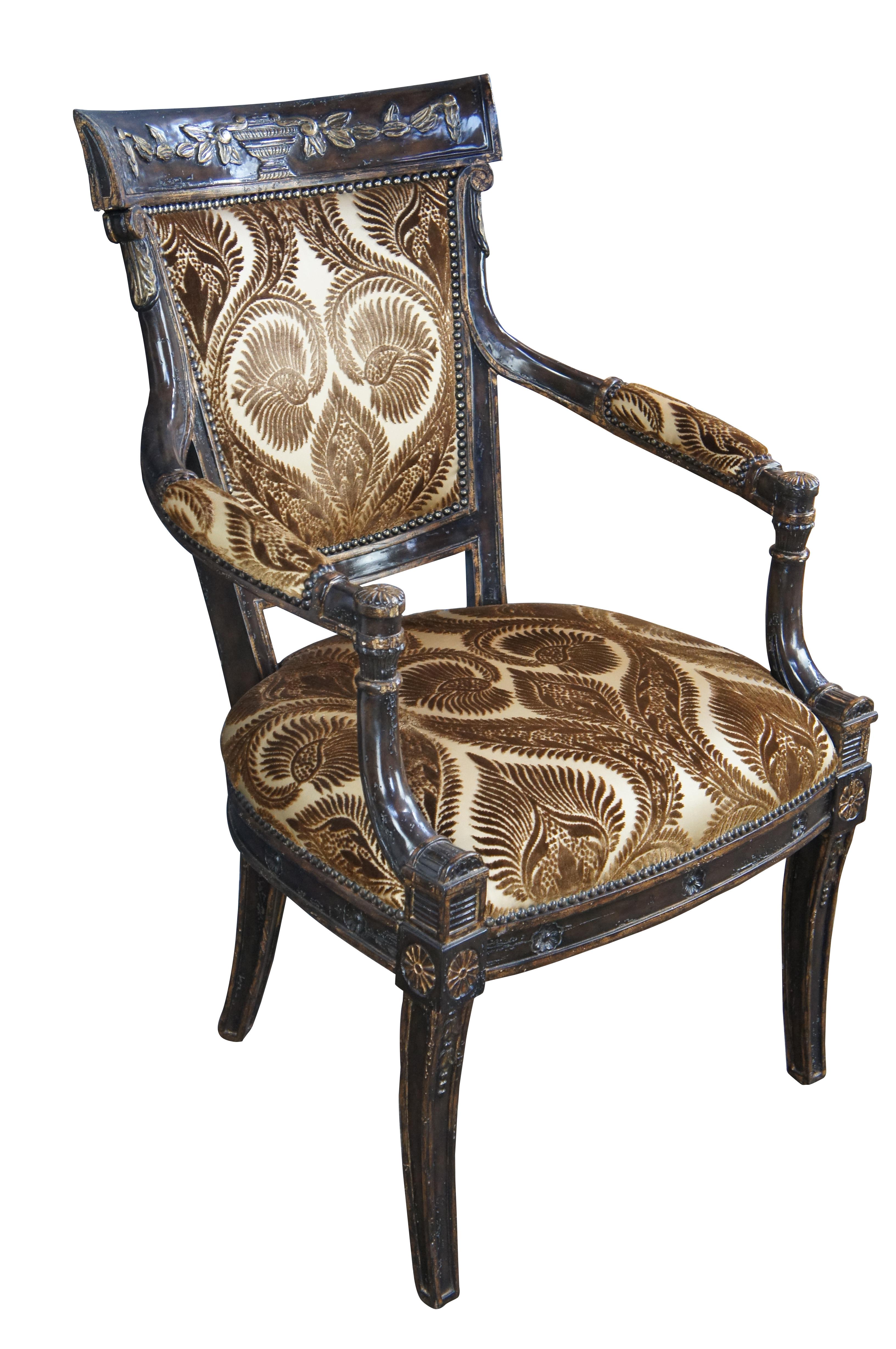 French Empire style arm chair by Marge Carson. Features a mahogany finished and distressed frame with an intriguing brown / gold foliate upholstered seat and back. Crest rail is contoured with a carved Grecian urn at the center surrounded by foliate