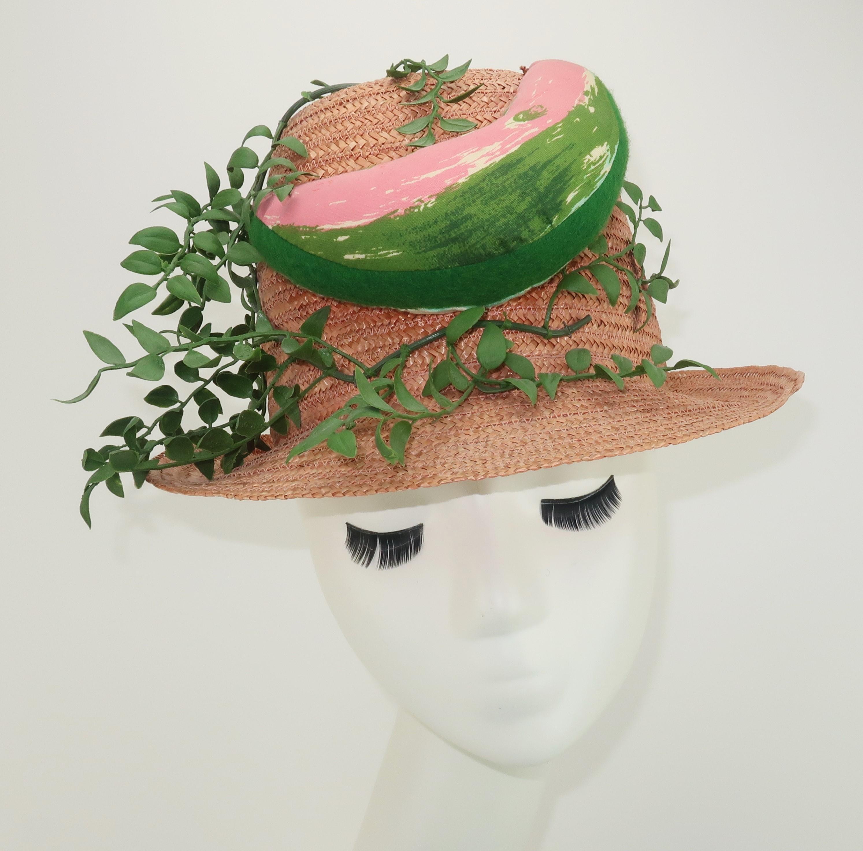 1960's novelty straw hat by Margie Webb Designs, California Accessories.  The fleshtone pink straw body is made in Italy and has a trilby style silhouette whimsically decorated with a stuffed fabric watermelon slice and faux green foliage.  A fun