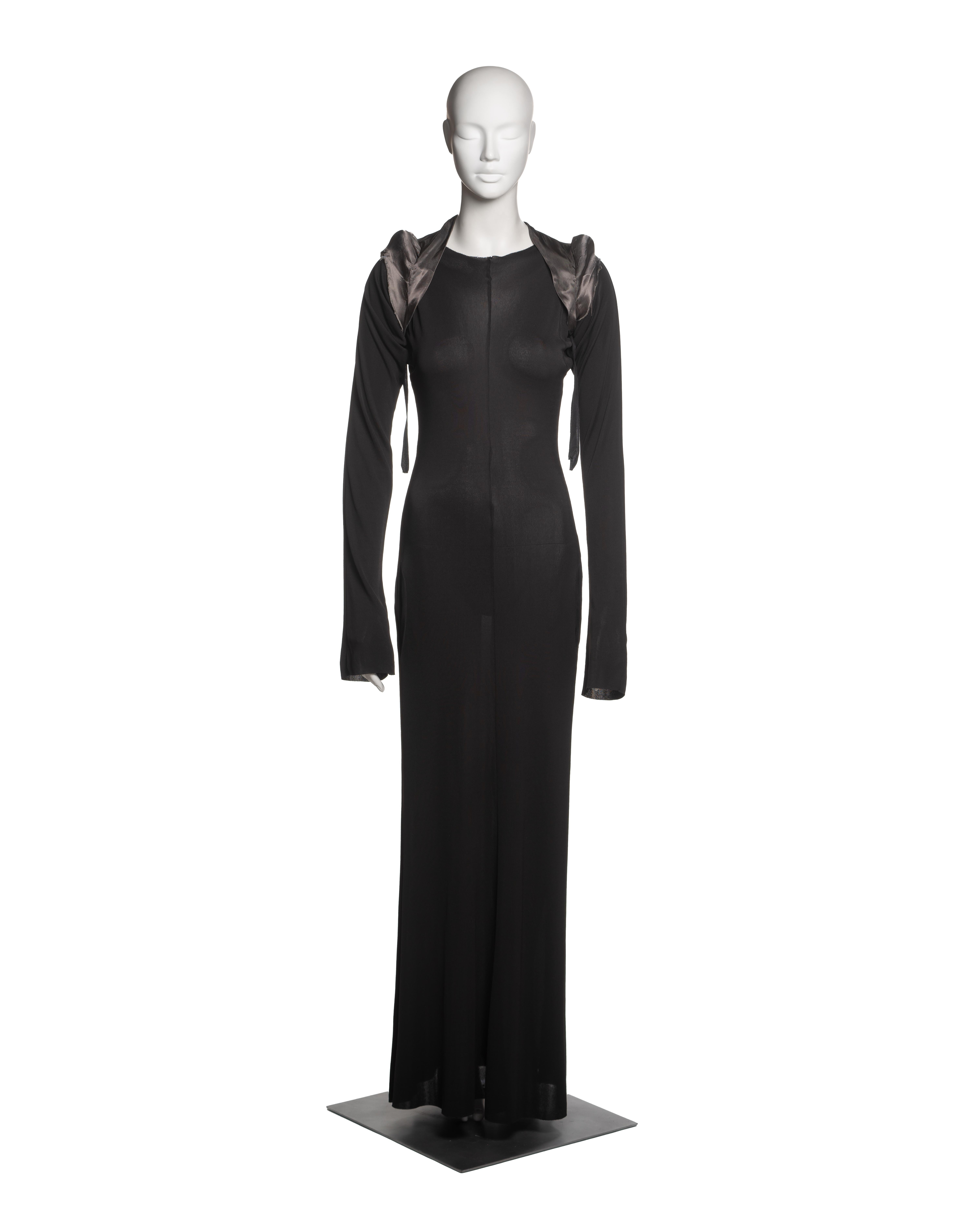 This Martin Margiela ensemble from Fall-Winter 1992 consists of a black jersey dress and a separate padded bolero, known as a cigarette shoulder in Margiela’s lexicon. The bolero, constructed from smoky grey satin with internal padding, sits atop