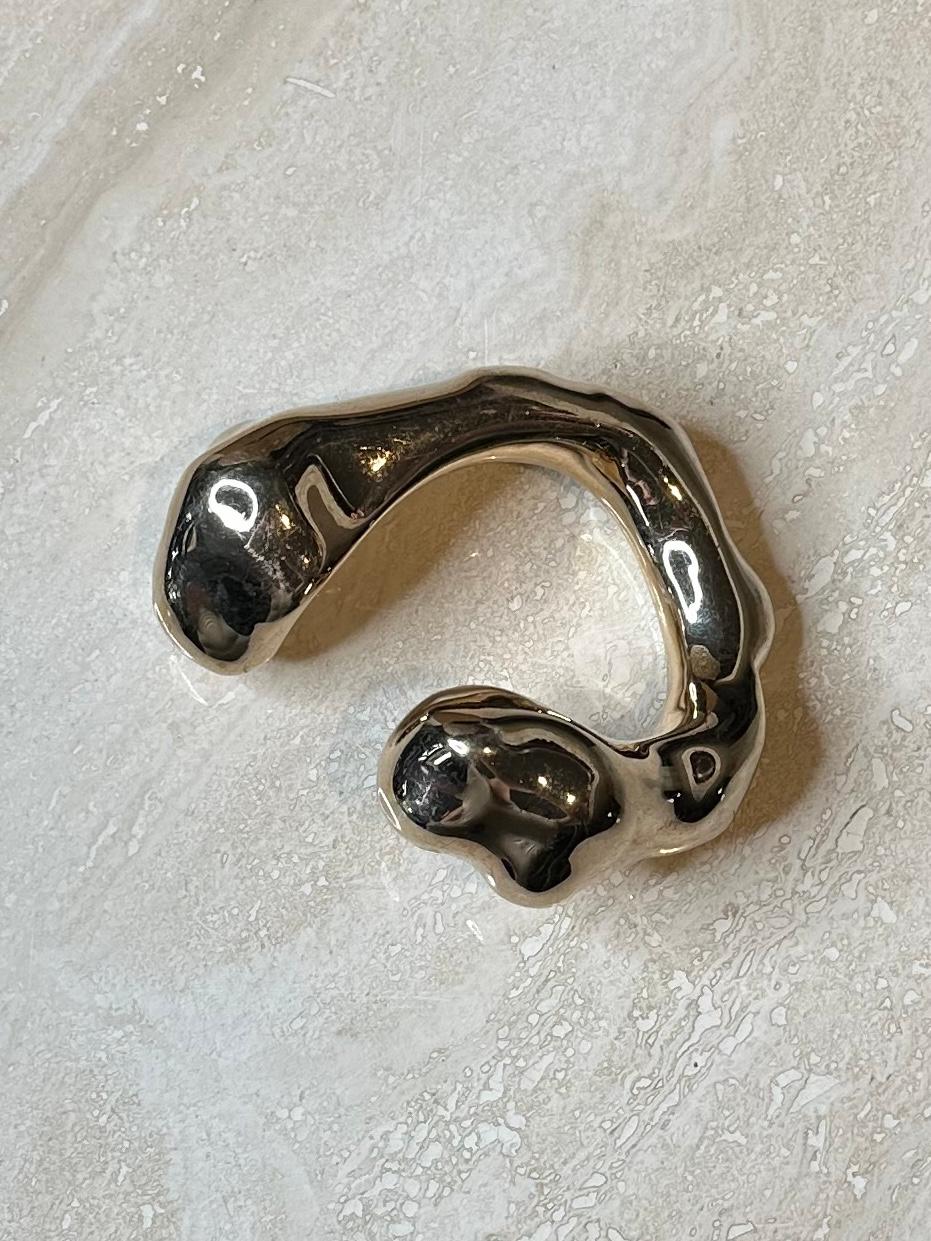 Le bracelet abstrait en or Margiela est un bijou audacieux, artistique et avant-gardiste qui se distingue par son design sculptural et asymétrique. Fabriqué à partir de matériaux de haute qualité et doté d'une finition dorée, il allie luxe et design