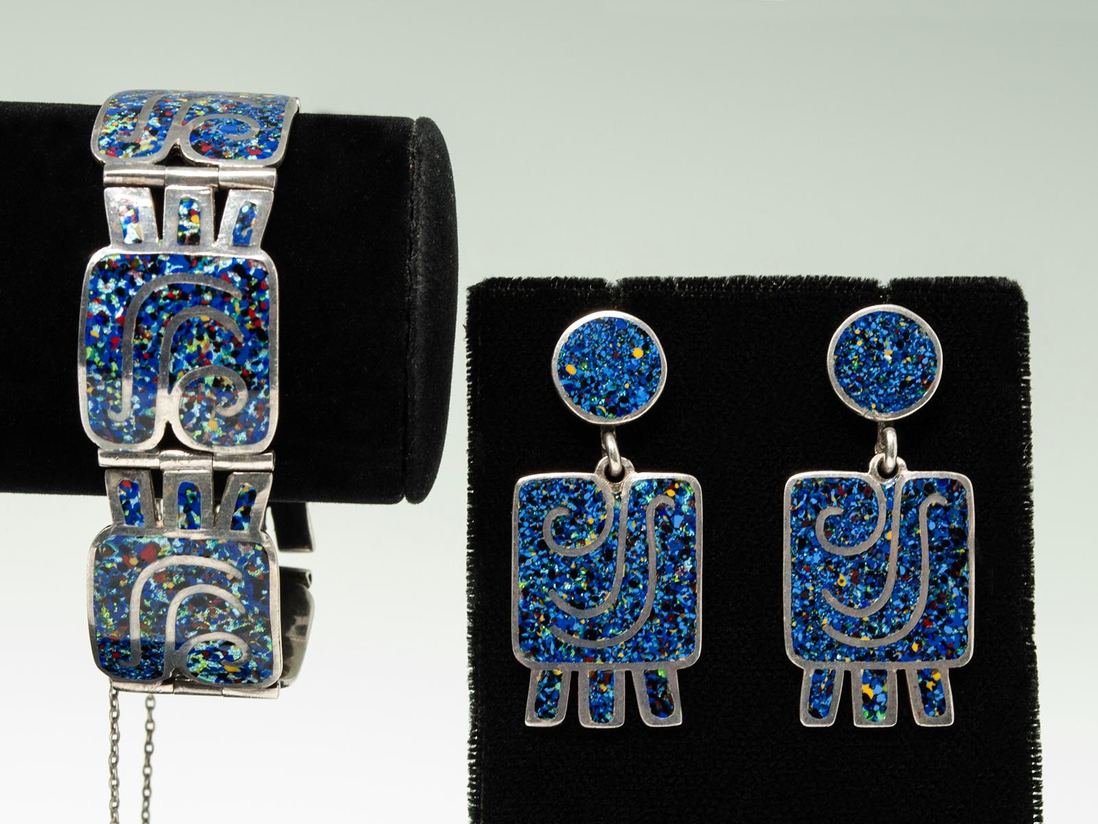 Add a splash of color and mid-century flair to your wardrobe with this Margot de Taxco bracelet and earring set. Crafted between 1948 and 1955, this design features a striking blue confetti enamel, set in a sleek silver frame that showcases Margot's