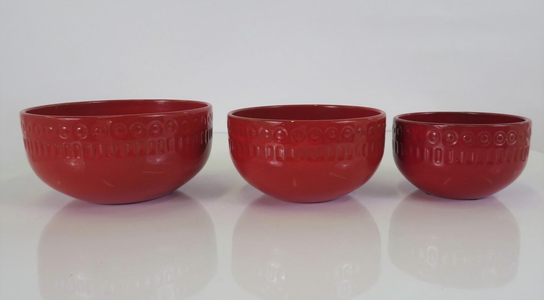 Mari Simmulson ( 1911 - 2007 ) for Upsala - Ekeby, Sweden, a set of nesting ceramic bowls. These tomato red utilitarian bowls are decorated with a band of an incised pattern of circles and vertical lines around their tops and center. These pieces