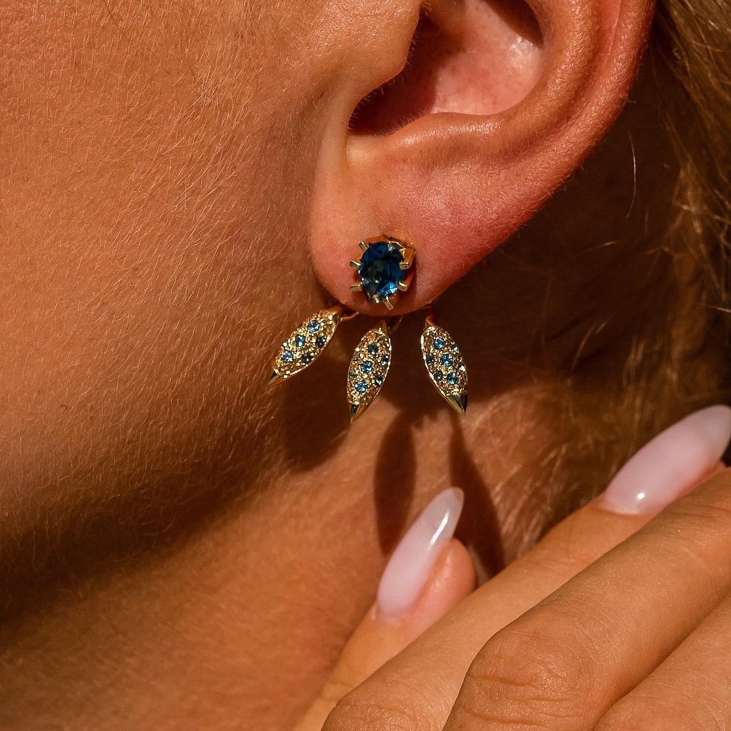 The ‘Grain’, ear jackets are crafted in 18K gold hallmarked in Cyprus. These impressive three part sculptural earrings come in a highly polished finish and feature a pair of separate London Blue Topaz studs totaling 1,0 Cts that can be worn