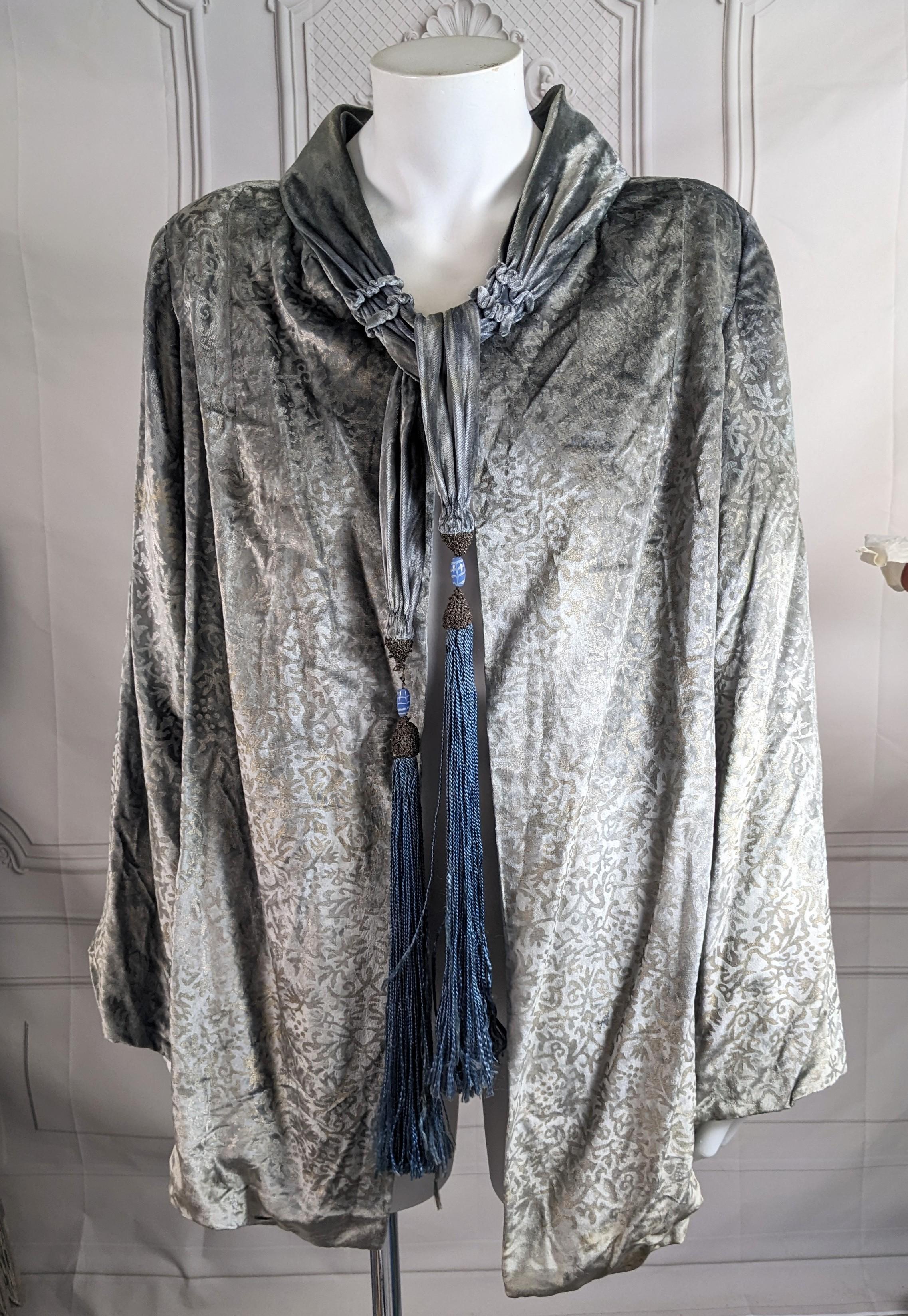 Maria Monaci Gallenga Chaqueta de noche de terciopelo de seda azul hielo de los años 20. Estampado general con un motivo foliado medieval en plata y oro. Cuello de terciopelo fruncido con lazos largos. Borlas de pasamanería doradas y de seda con