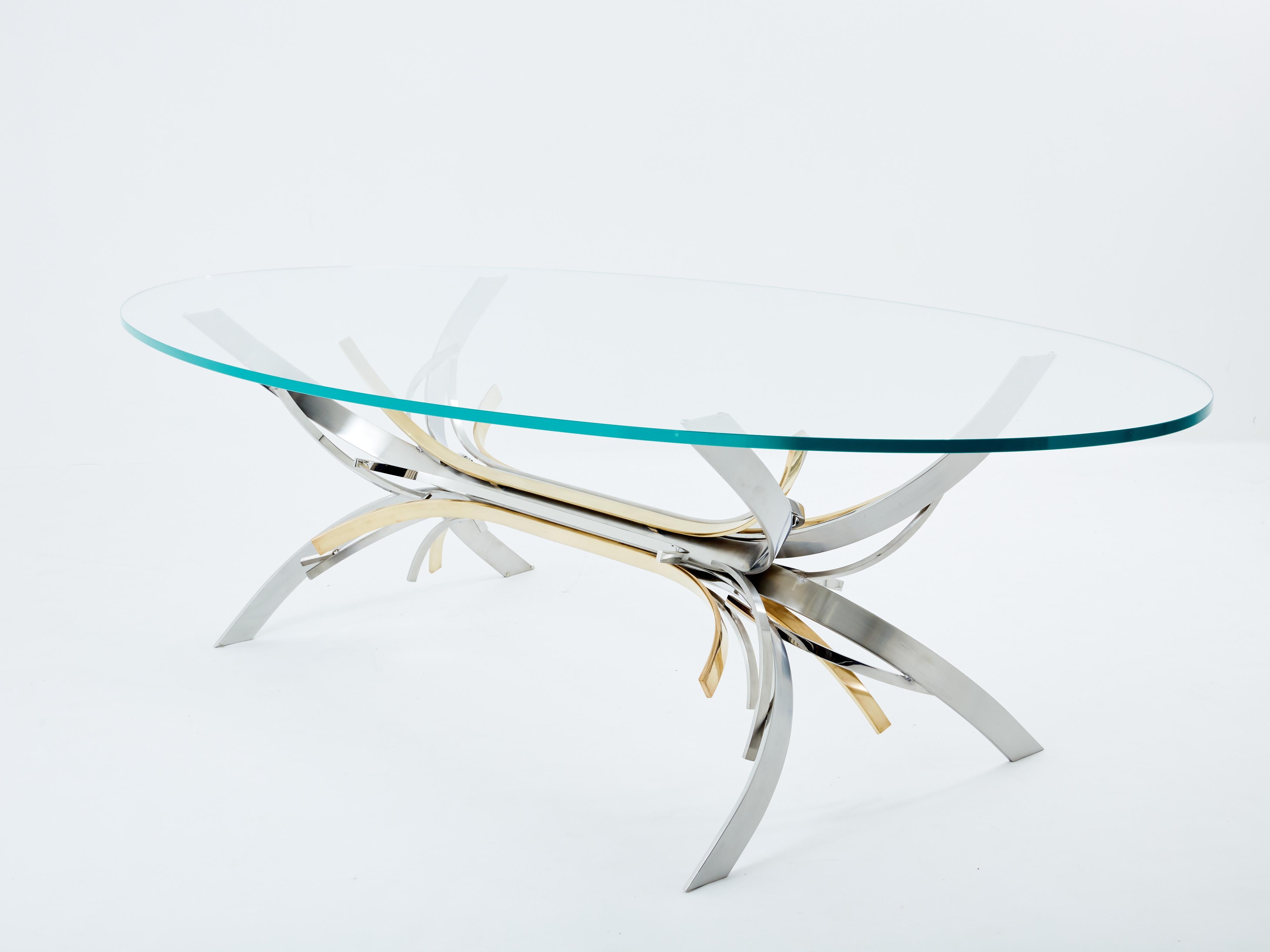 This dining table is a rare variation of French artist Maria Pergay's iconic Gerbe model, dating back to 1970. It features a cluster of flat and curved blades in polished steel, brushed steel, and polished brass, topped with an oval transparent