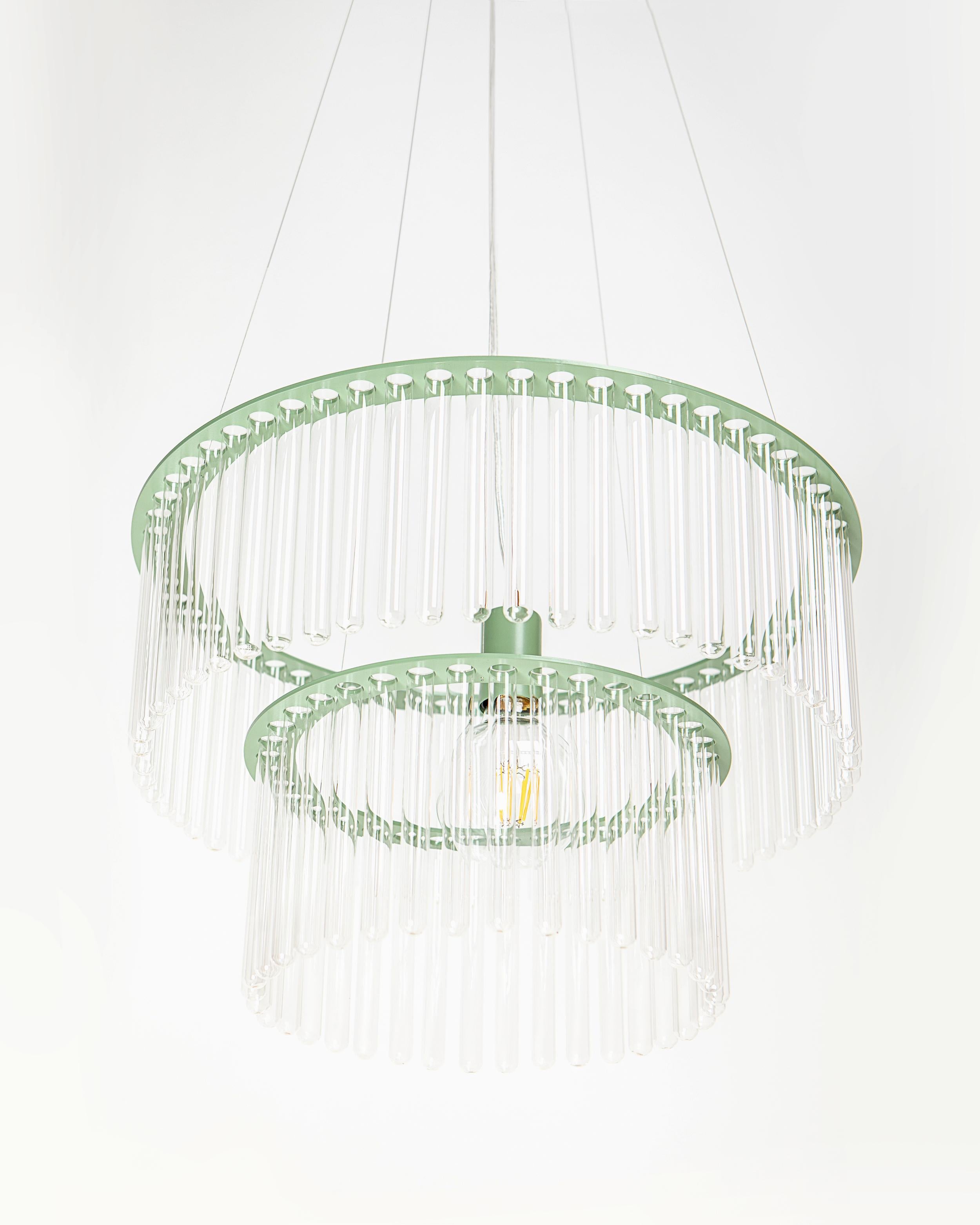 Il lampadario Maria S.C. è realizzato con provette da laboratorio, incastonate in due fasce di metallo. Il materiale sorprendente e la forma geometrica rendono questa lampada classica e moderna allo stesso tempo. Richiama le forme dell'Art Déco in