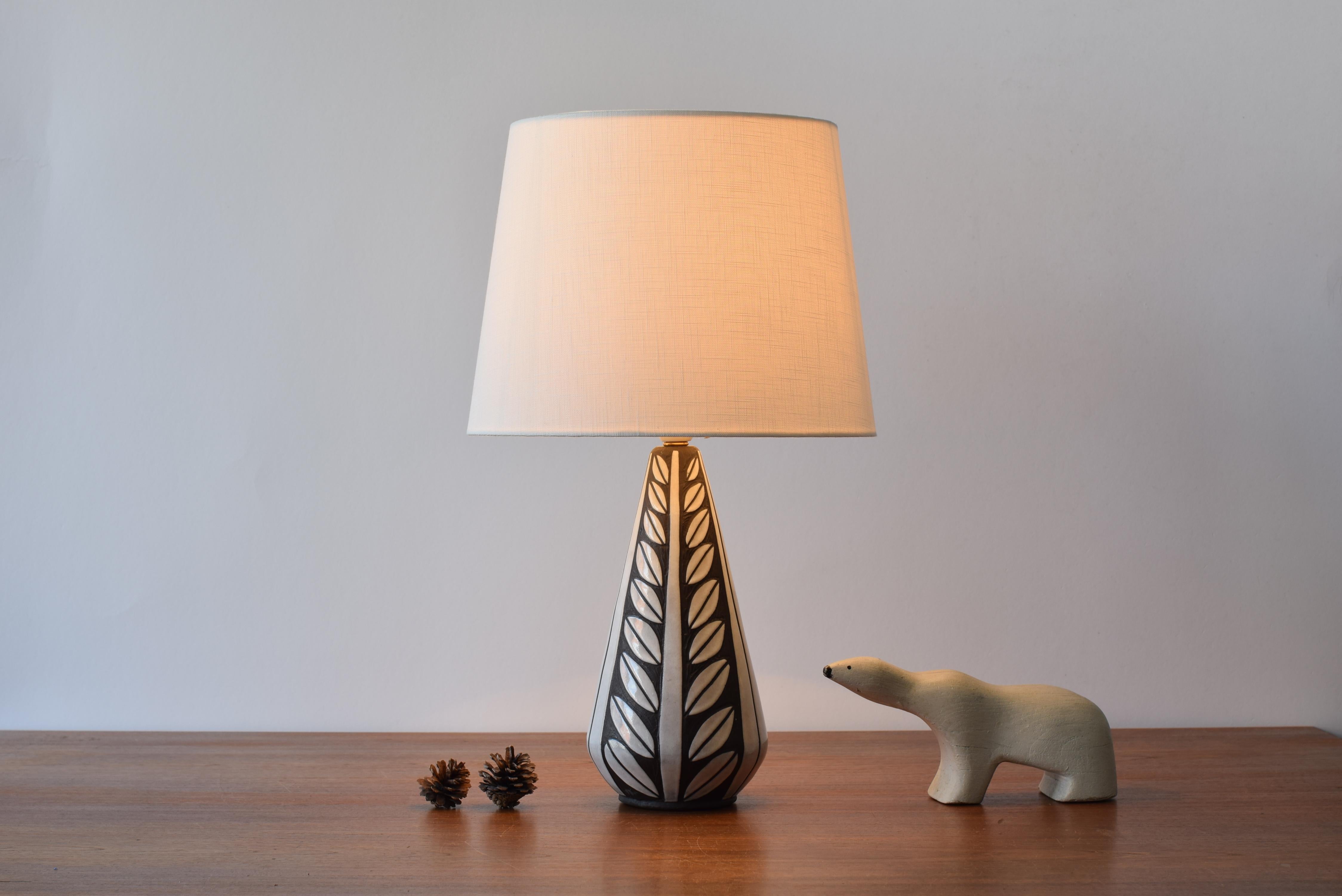 Danish midcentury ceramic table lamp designed by Marianne Starck for Michael Andersen & Søn (MA&S).
The lamp belongs to the Negro series - also called Tribal series - and shows a stylized leaf decor in sgraffito technique with white glaze