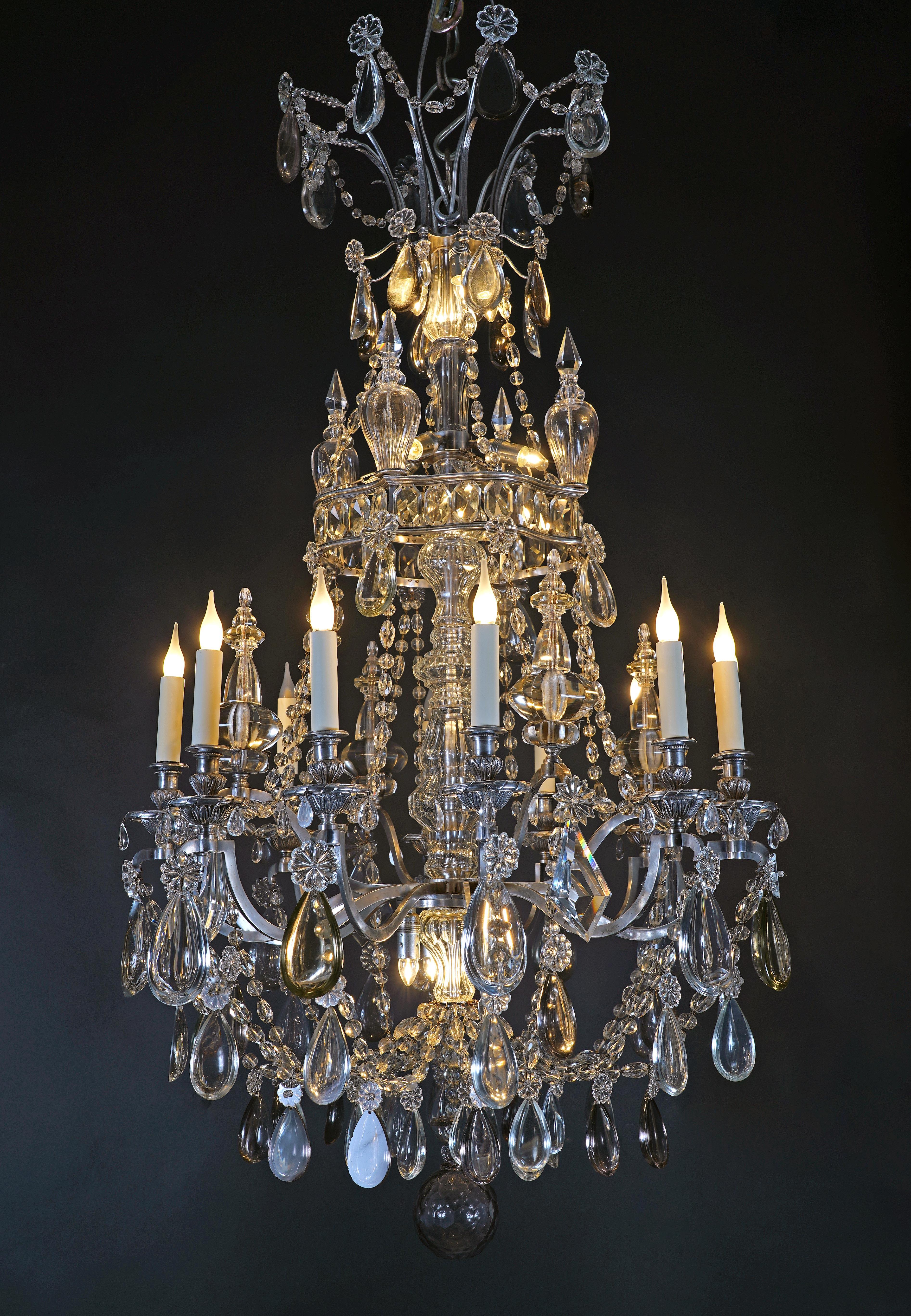 Bellissimo lampadario a balaustro di ispirazione Luigi XVI, con montatura in cristallo e bronzo argentato. Il fusto centrale, fatto di fili, è illuminato da 12 luci indirette e da 12 bracci luminosi che terminano in bobeches appoggiate su bacini di