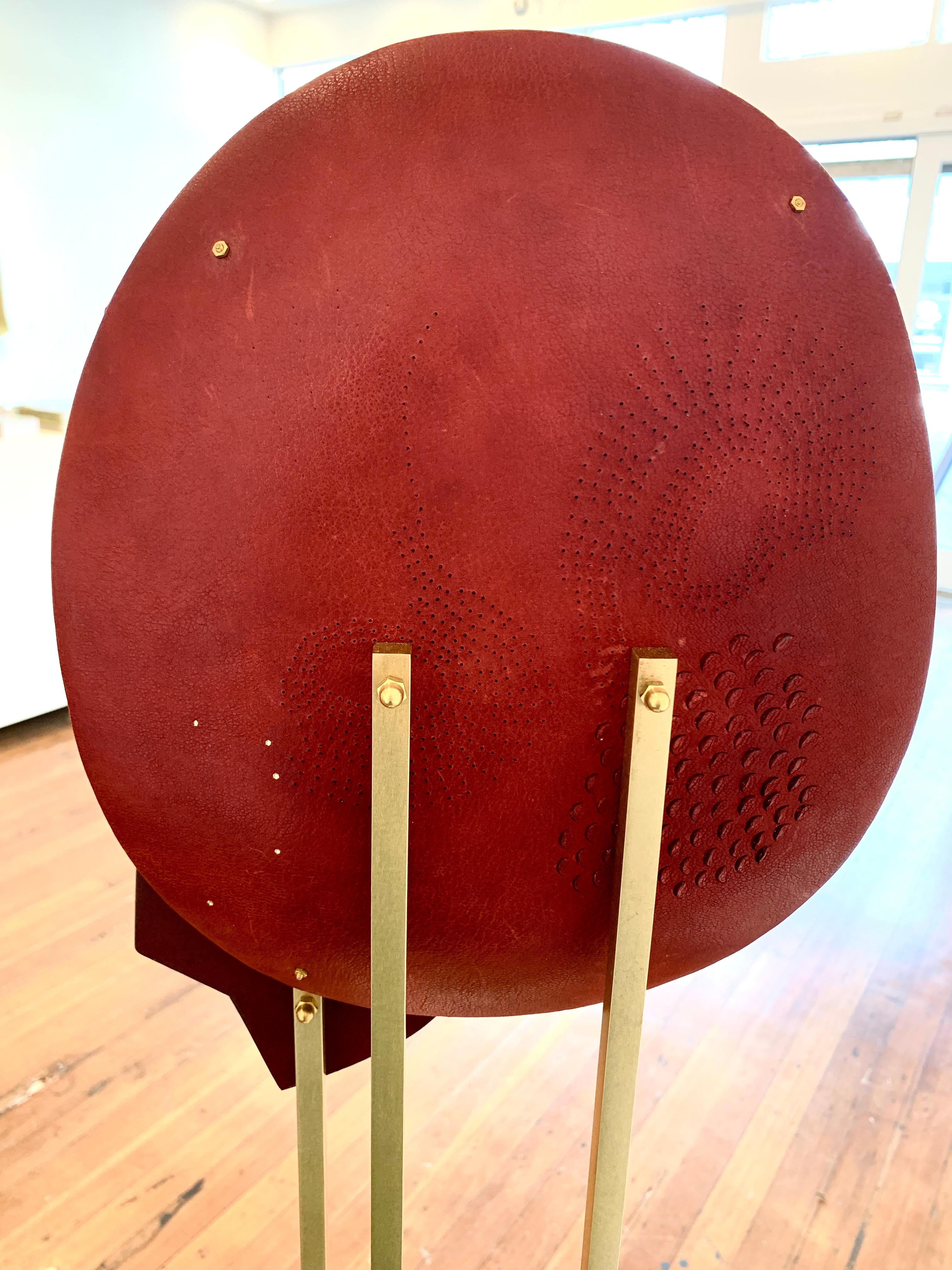 Questa scultura in pelle unica nel suo genere, con uno specchio tagliato a mano su una base in ottone, impiega diverse tecniche tra cui: doratura a caldo, ricamo con fili di rame, scarificazione, piercing e disegno a caldo, con accessori in metallo