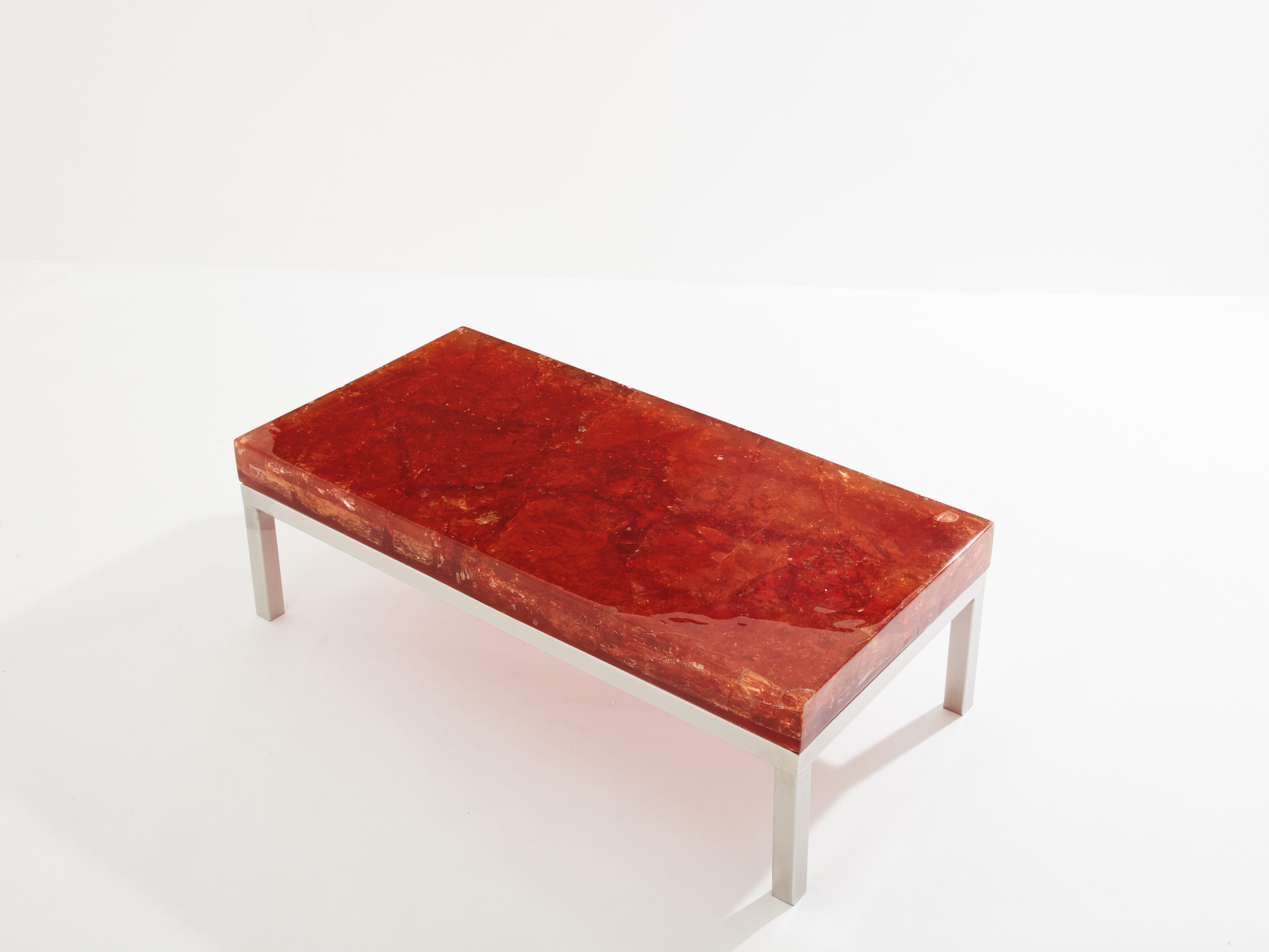 Cette table basse, conçue par Marie-Claude de Fouquières dans les années 1970, est une pièce remarquable. Son plateau est réalisé en résine fractale orange ambrée aux reflets dorés, rappelant le cosmos. La résine fractale est le résultat d'un