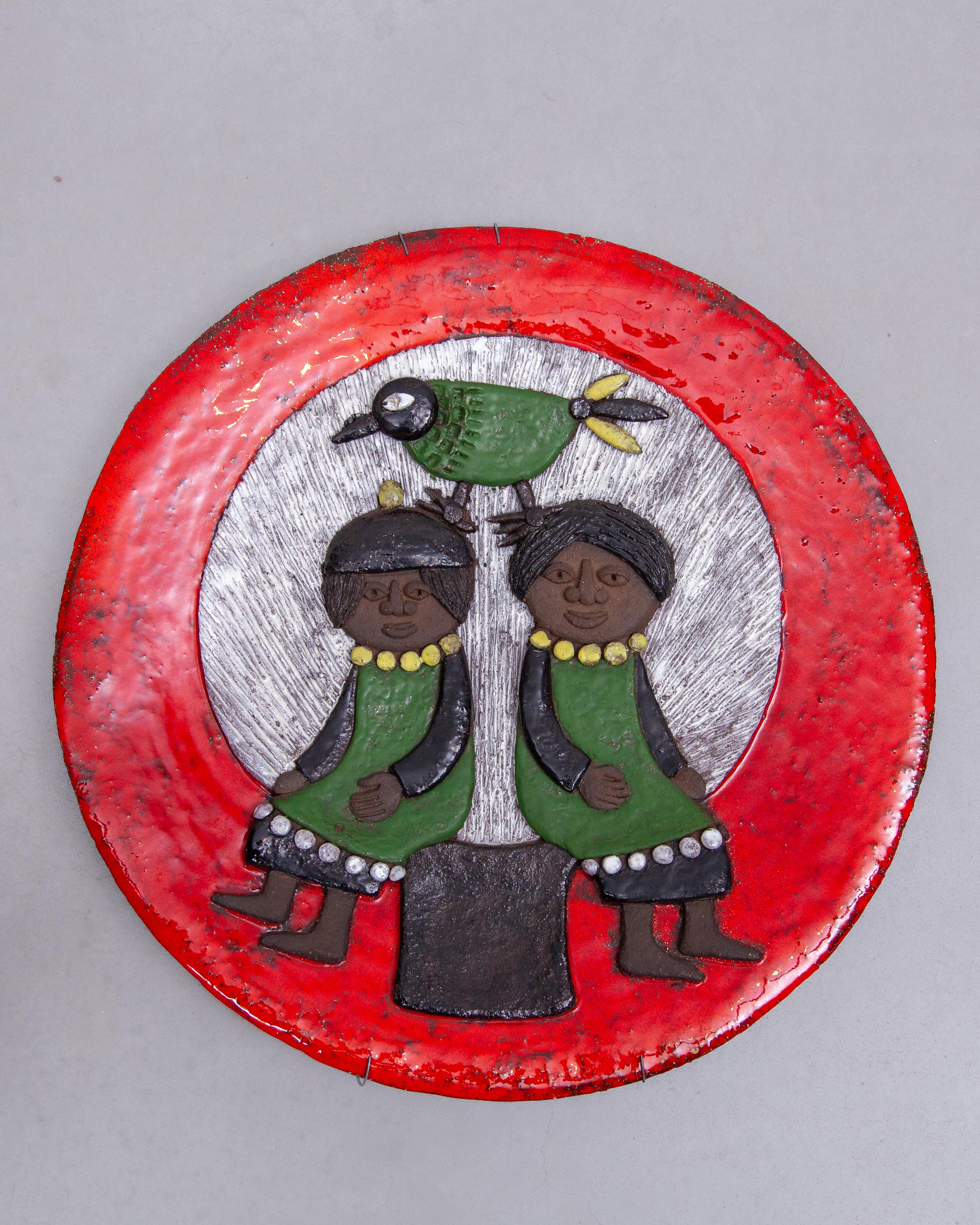 Beautiful expressive ceramic wall art round plate by Marie Henriette Bataille for Atelier Dour, Belgium, Belgium, 1960s, signed. A ceramic plate with two women seated by a tree with a bird in the tree behind the rising sun, in relief, glazed in