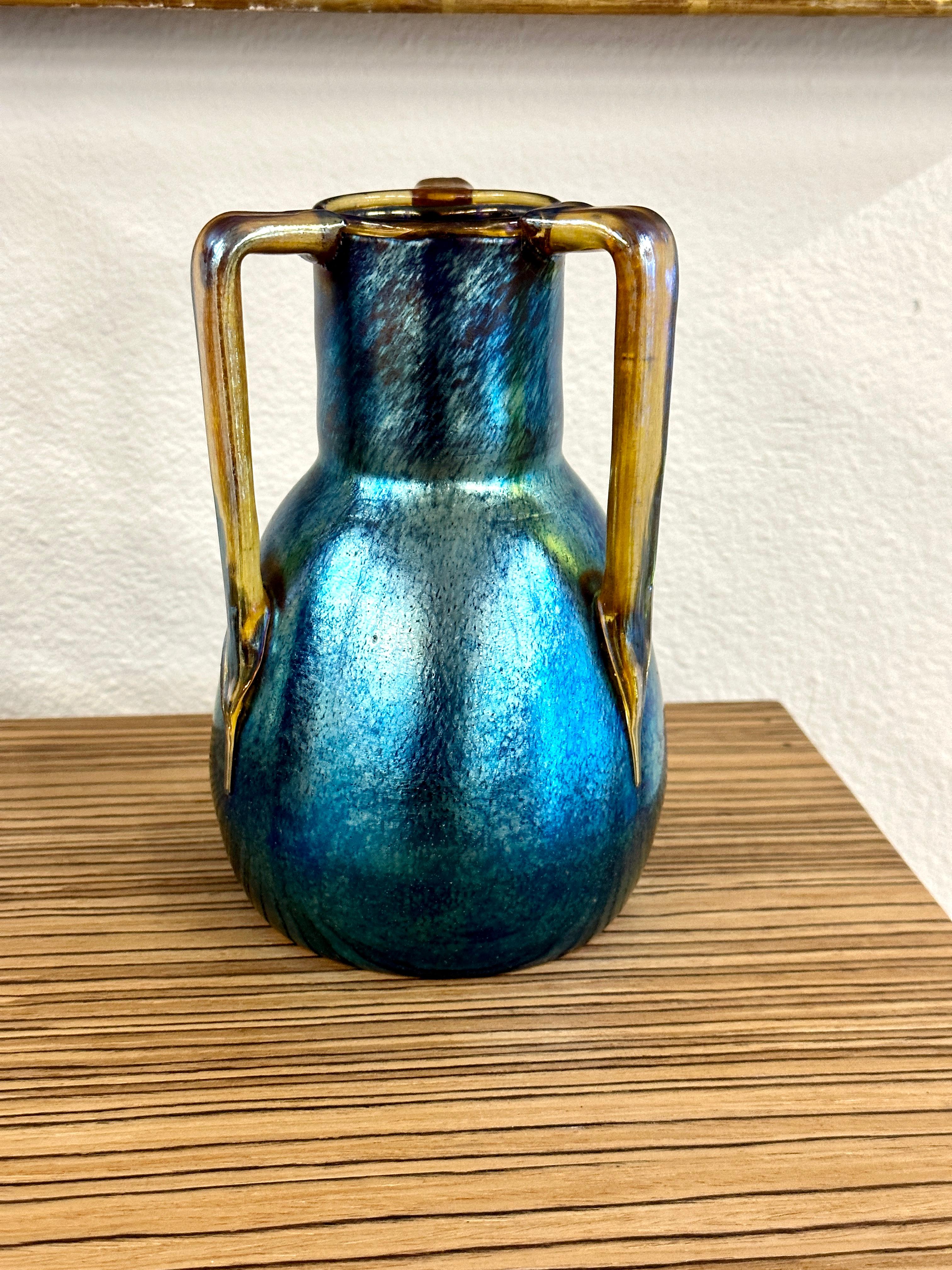 Beautiful Loetz iridescent glass three handled vase by Marie Kirschner. Lovely contrasting colors. Weve photographed it in different light to try and capture it's shimmer and beauty.
In good condition. A brief bio of the artist from the Loetz. com
