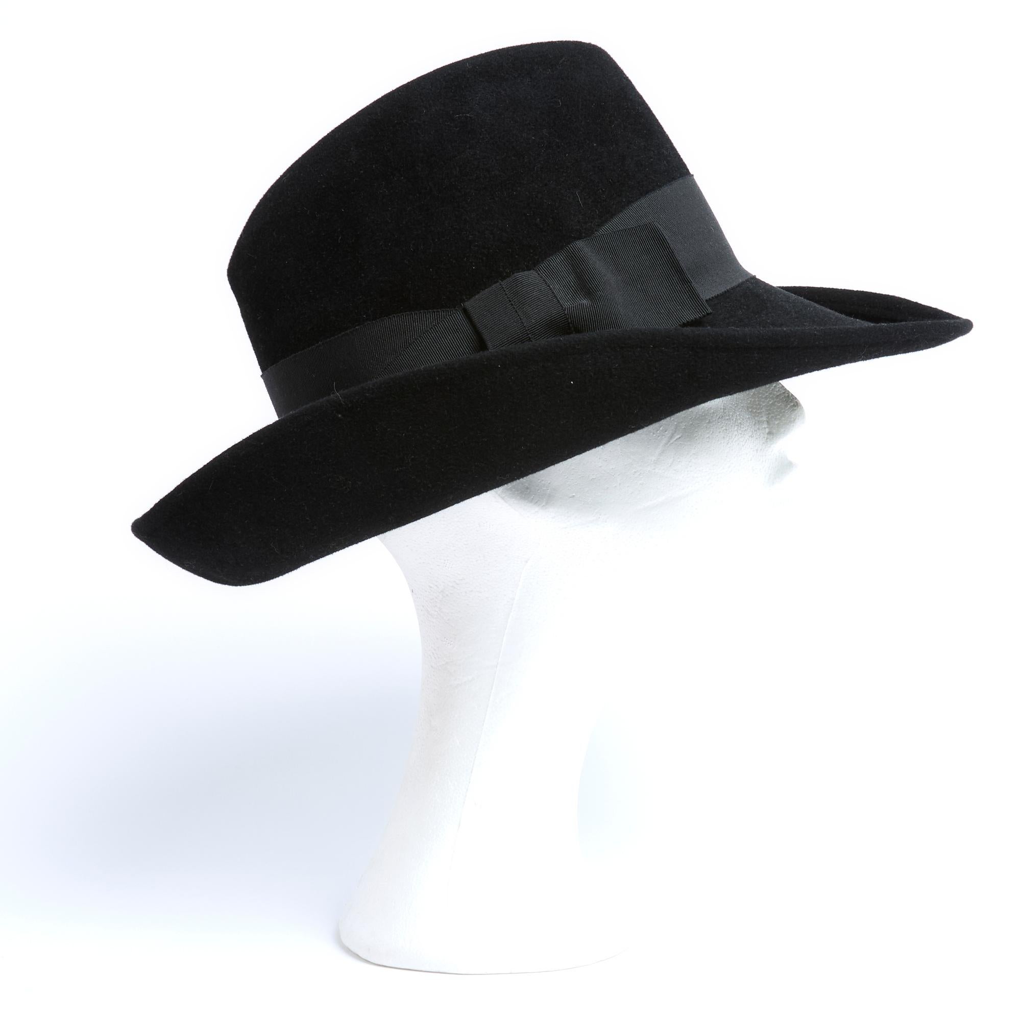 Marie Mercié übergroßer, leicht asymmetrischer Hut im Fedora-Stil aus schwarzem Wollfilz mit breiter Krempe, Band und Schleife aus koordinierter Ripsbandborte. Kein Größenetikett, aber die Beschläge deuten auf L oder einen Kopfumfang von 58 cm hin.