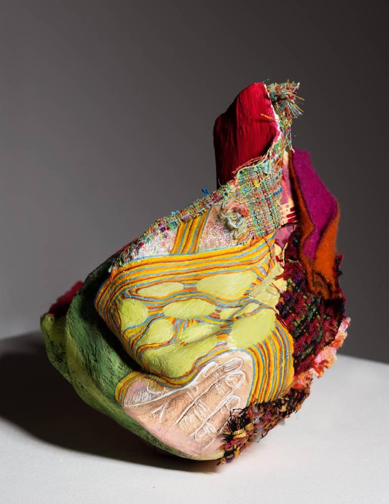 Red, the title and color of the sculpture, has a spiky orange heart at its center. Textiles and painted trompe l’oeil embellish the outer surfaces. The artist’s work explores the marriage of painting and sculpture in this hybrid. Ambiguous yet