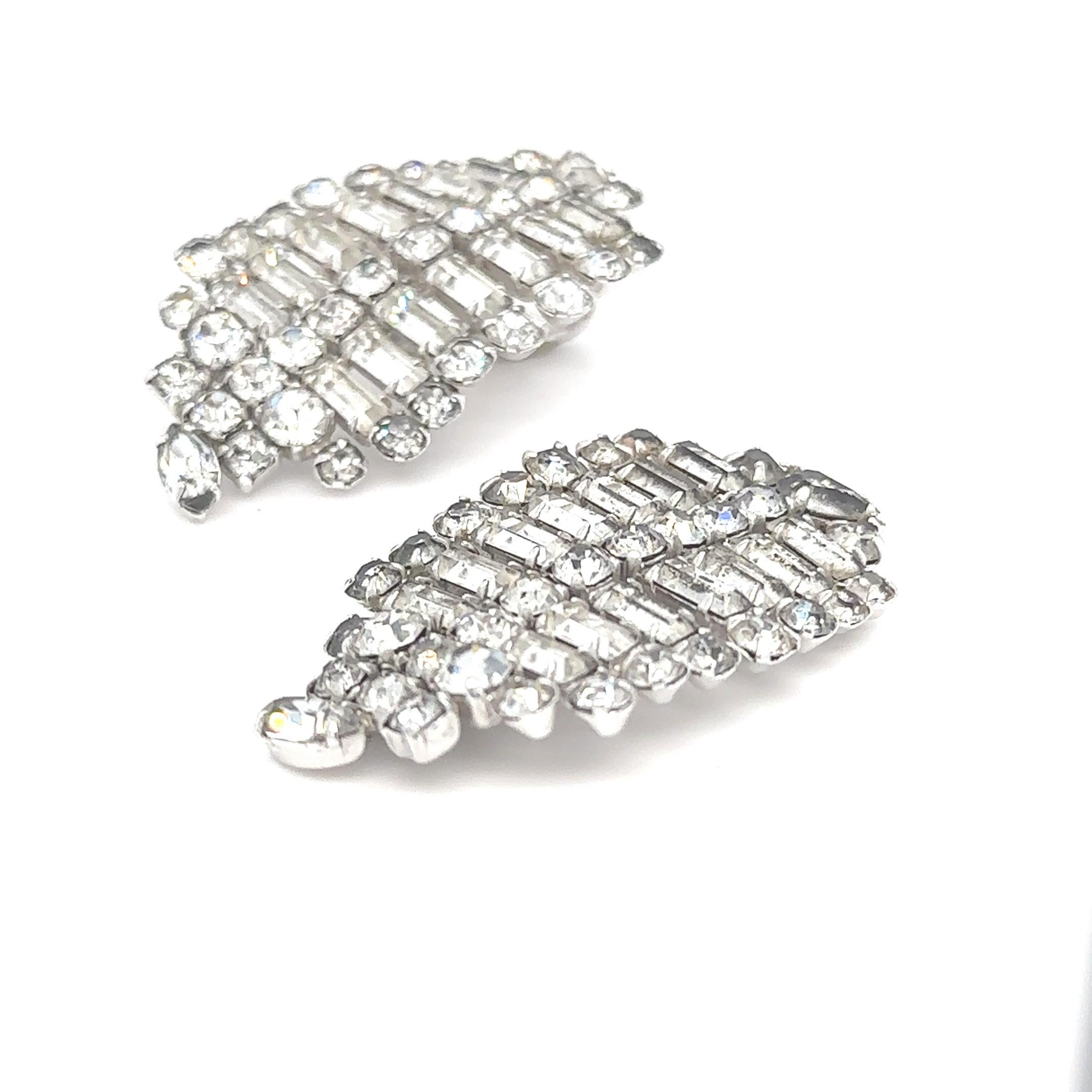 Clip on earrings featuring parallel rows of alternating round and emerald prong set rhinestones. 
One earring is lacking the clip. 
The earrings are very similar in style to those worn by Monroe in the film Don't Bother To Knock and in photographs