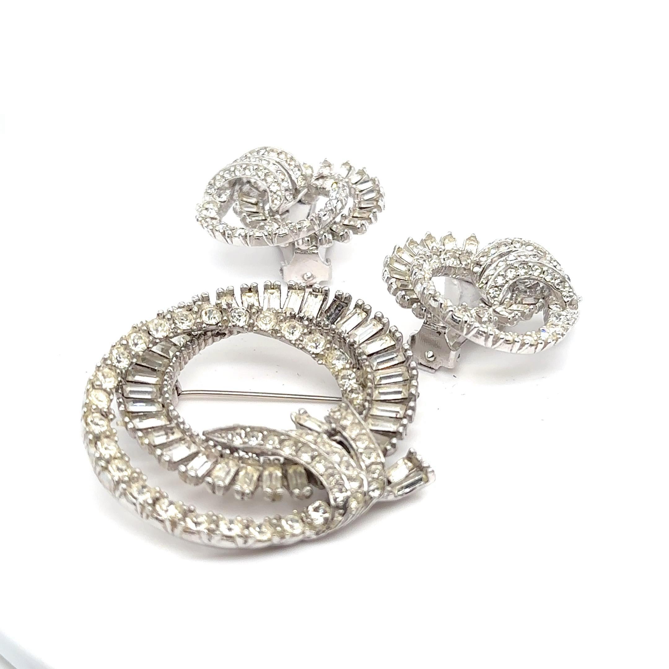 Stick pin brooch and earrings in a swirling design of rhinestones. 
Earrings are marked 
