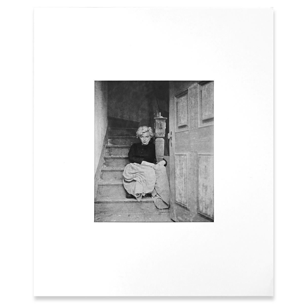 Atypical photo of Marilyn Monroe on dusty stairs in a shabby porch. Devoid of any form of glamor the natural beauty of the moviestar remains proudly intact. Dressed in a black lace top and seemingly with a package of rags on her lap, she looks