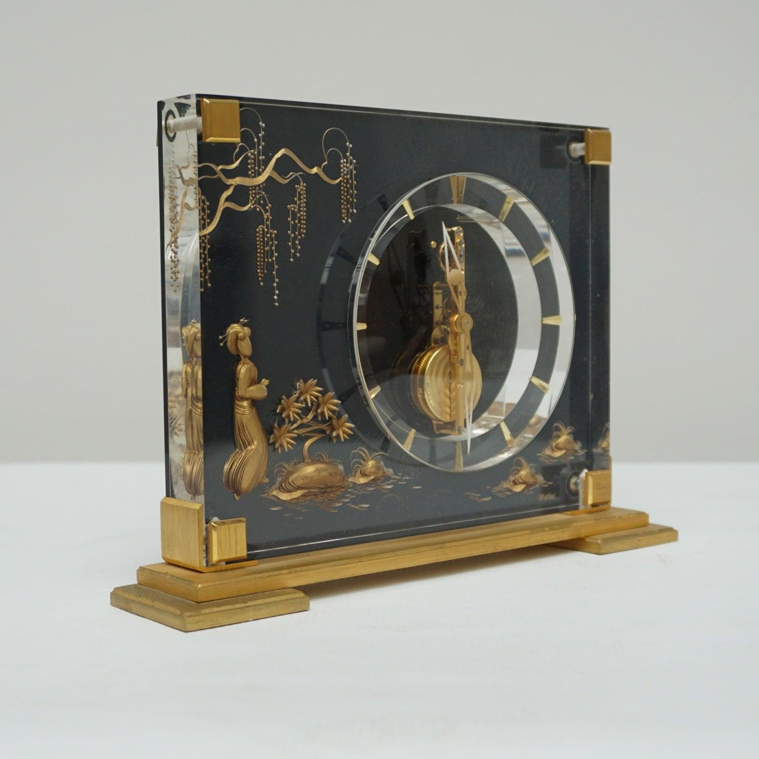 A mid-century Jaeger-LeCoultre mantel clock in a Lucite case with inset brass decoration featuring a young girl amongst the lily pads with an overhanging branch above. Set over a gilded Brass stepped base. Eight day movement by Jaeger-LeCoultre with