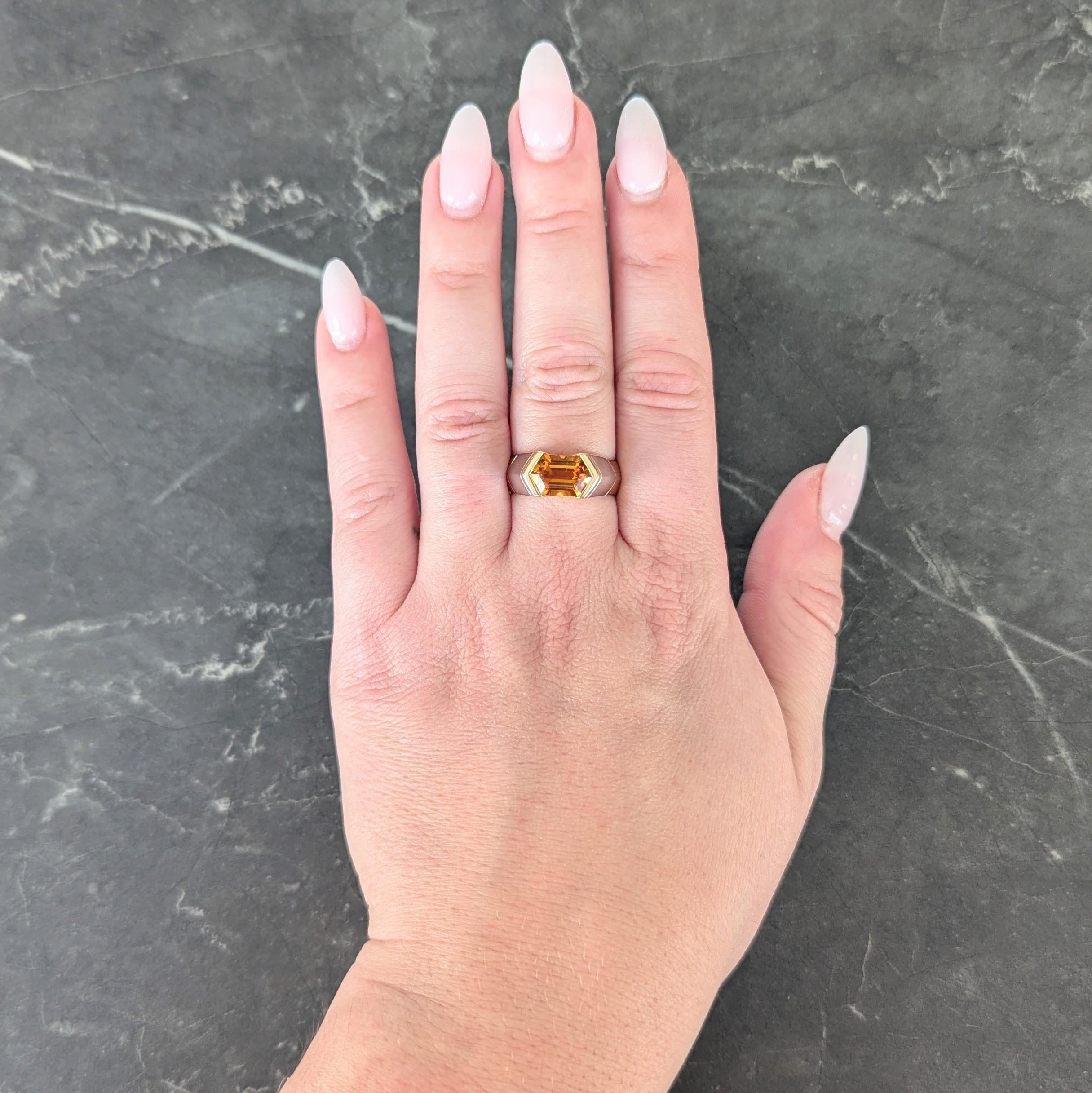 Centering an elongated hexagonal cut citrine weighing approximately 2.15 carats
Transparent medium orange in color and bar set east to west
Flanked by knife edge chevron motif shoulders
Comprised of yellow and white gold segments
Completed by high