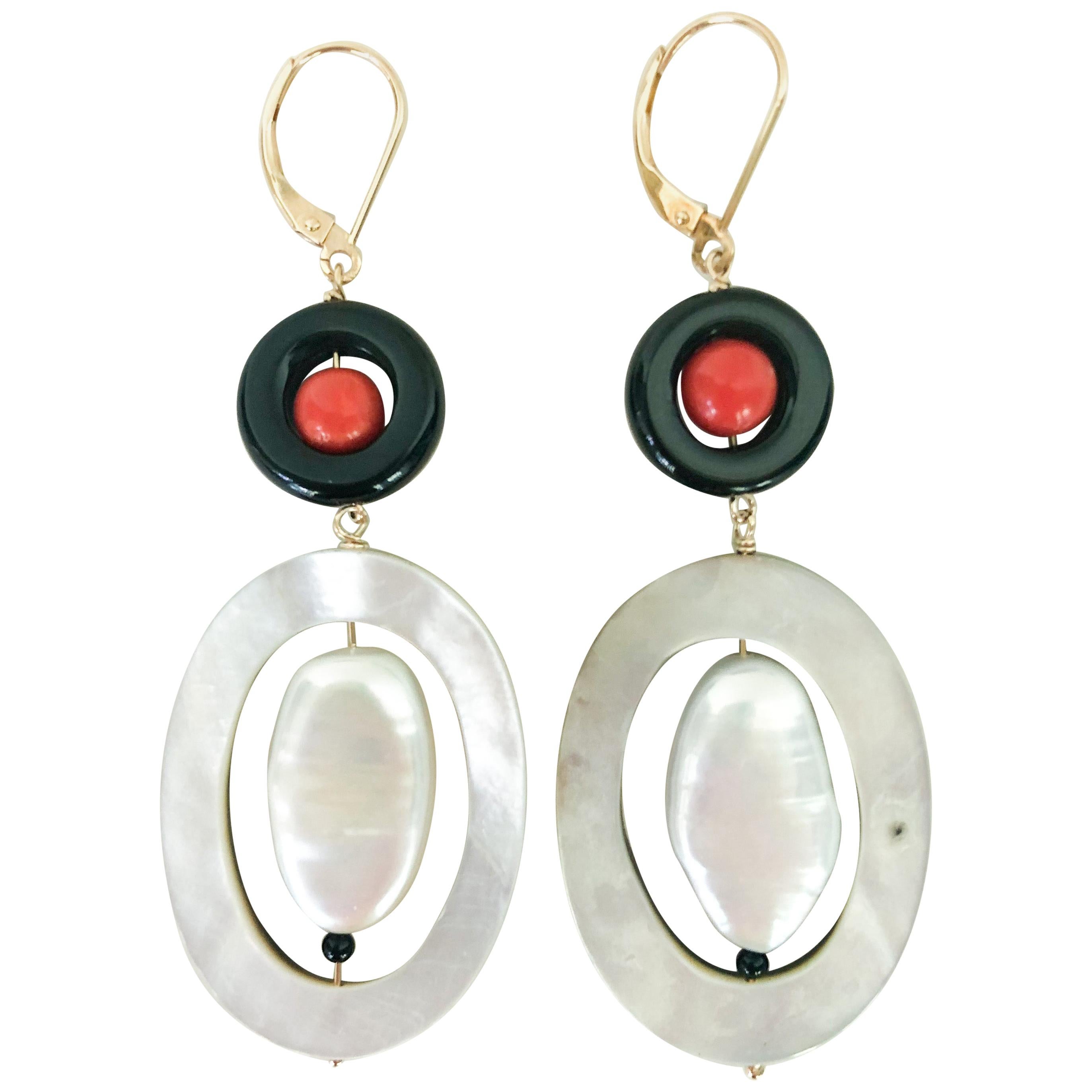 These unique art deco style earrings are made with a coral bead enclosed in an onyx ring, and a flat oval pearl enclosed in a mother of pearl oval ring. The wiring is made of 14k yellow gold and 14k yellow gold lever backs. The earrings are about
