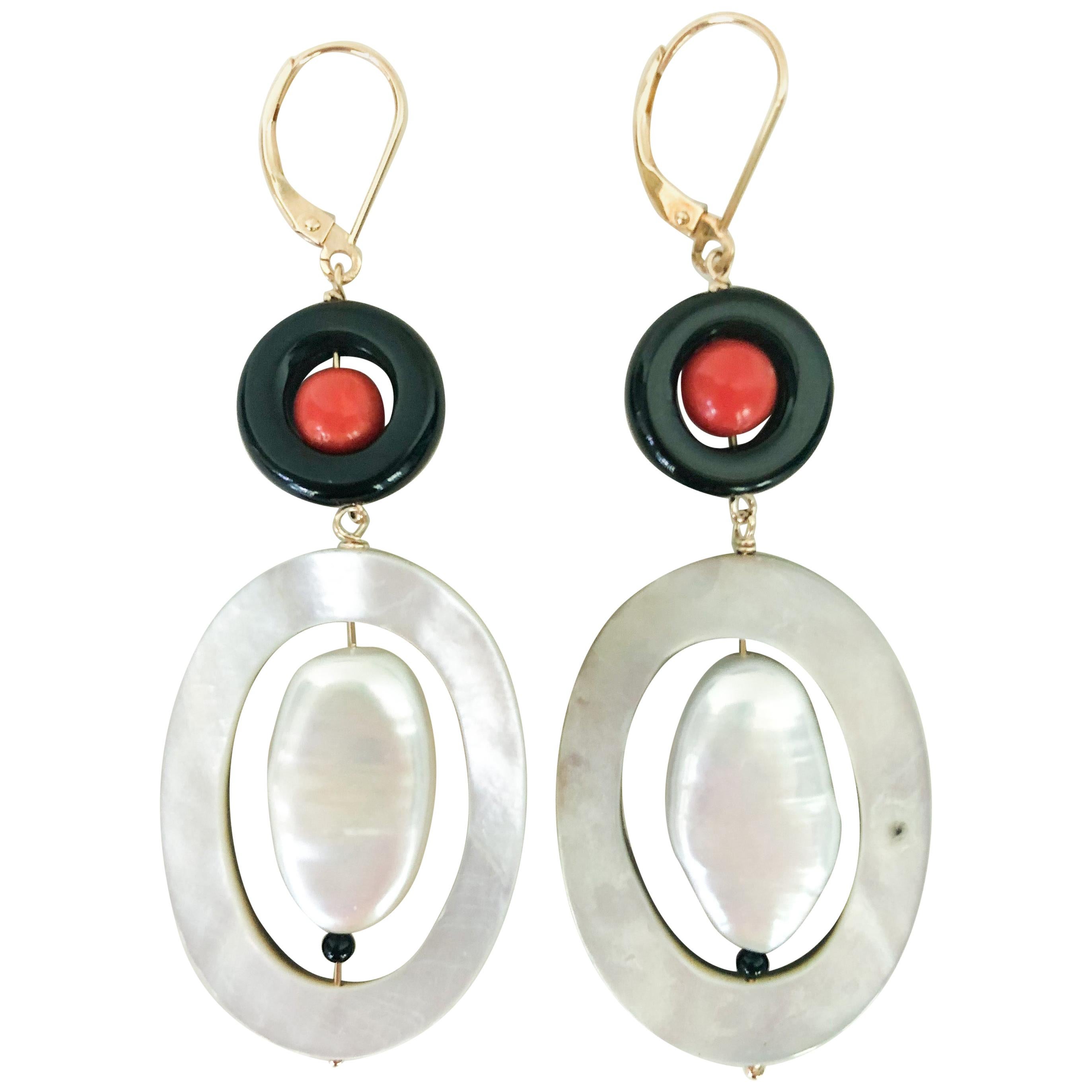 Questi orecchini unici in stile art déco sono realizzati con una perla di corallo racchiusa in un anello di onice e una perla ovale piatta racchiusa in un anello ovale di madreperla. Il cablaggio è realizzato in oro giallo 14 carati e i fermi a leva