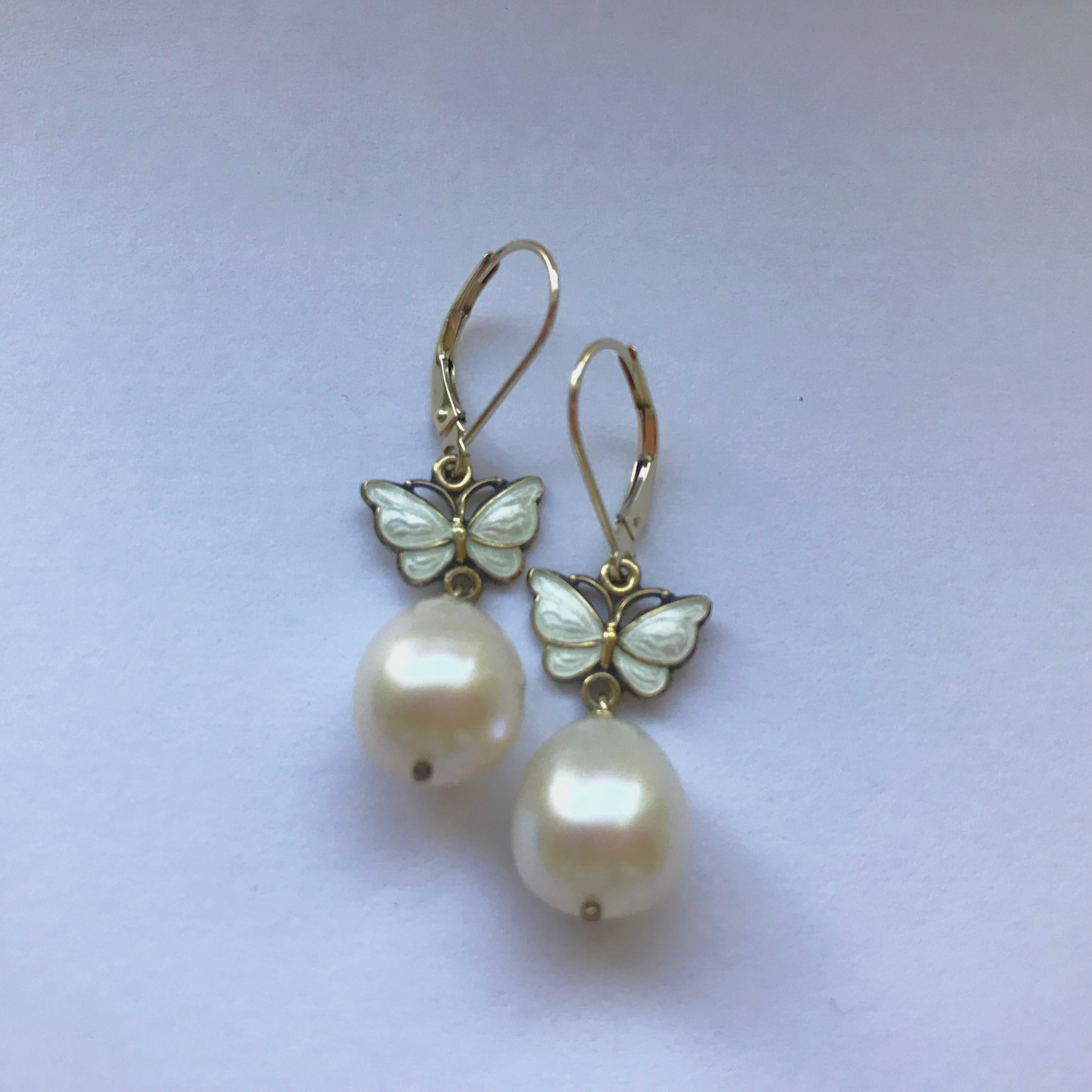 These earrings are perfect for a beautiful winter day out. A vintage butterfly (c.1950s) with fine white enamel hangs from a 14k yellow gold earring and finished with a large drop-shaped pearl. The earrings hang 1.5 inches in length, highlighting