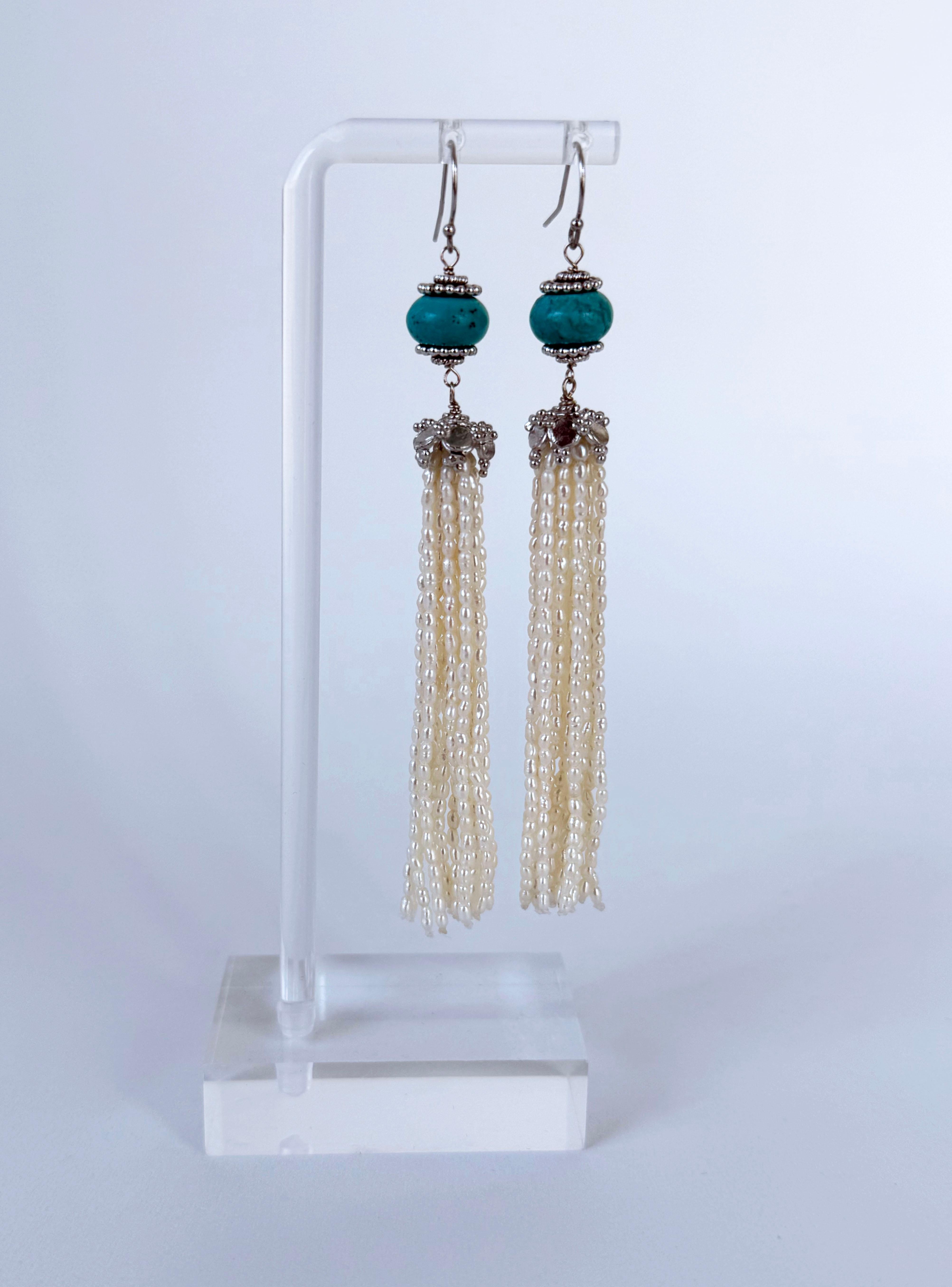 A stunning pair of Earrings.
This pair is made with vibrant Turquoise which are encapsulated between two Silver cups from which a decorative Silver Cup and long strands of Seed Pearls hang. A very fun elegant pair with a beautiful pop of Blue.