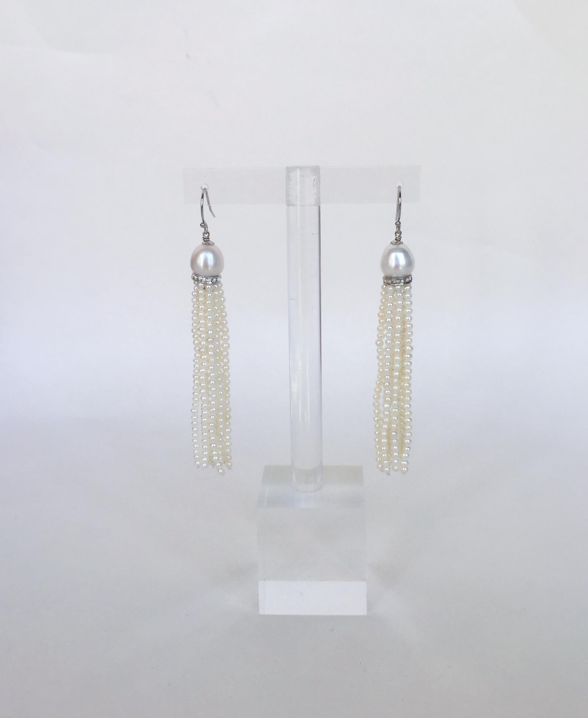Questi orecchini con nappe di perle bianche e diamanti in argento e oro bianco 14k sono eleganti.  I fili di perle bianche quasi perfettamente rotonde sono tenuti insieme da un tondo d'argento rodiato incrostato di diamanti. In cima al tondo si