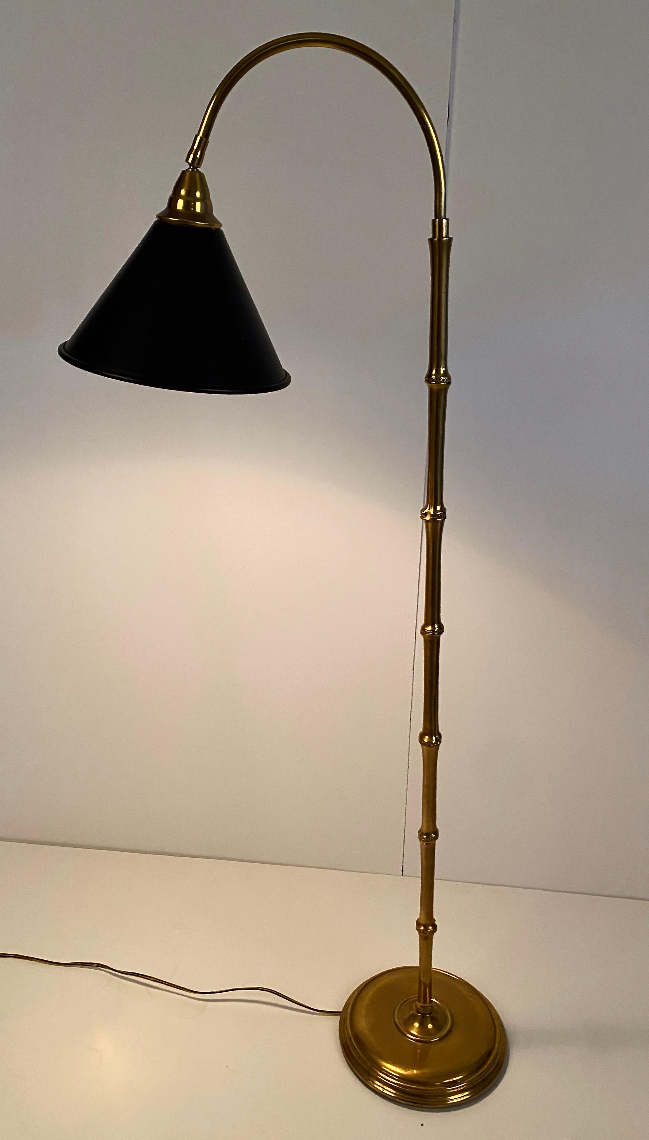 Handsome standing lamp with great functionality, designed by Mario Buatta for Frederick Cooper. Substantial brass base with elegant faux bamboo rod curves to hold a conical metal shade. The shade is attached to the lamp by a universal joint which