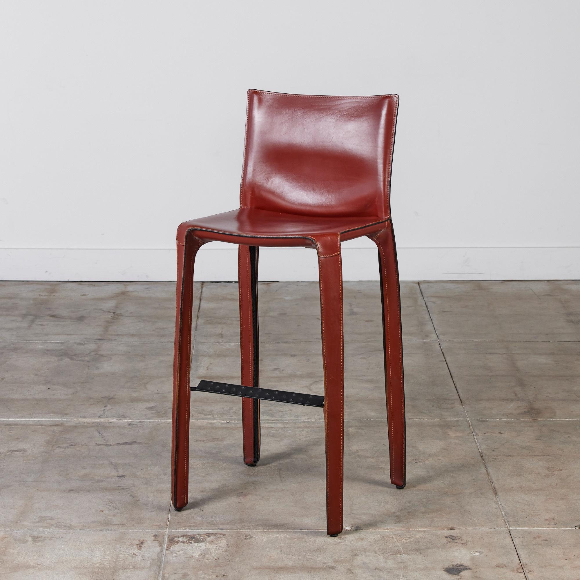 This iconic design by Mario Bellini for Cassina c.1970s, Italy, features the original deep red saddle leather which is wrapped atop a steel frame. The back legs feature a black zippered detail. A black textured footrest runs along the front of the